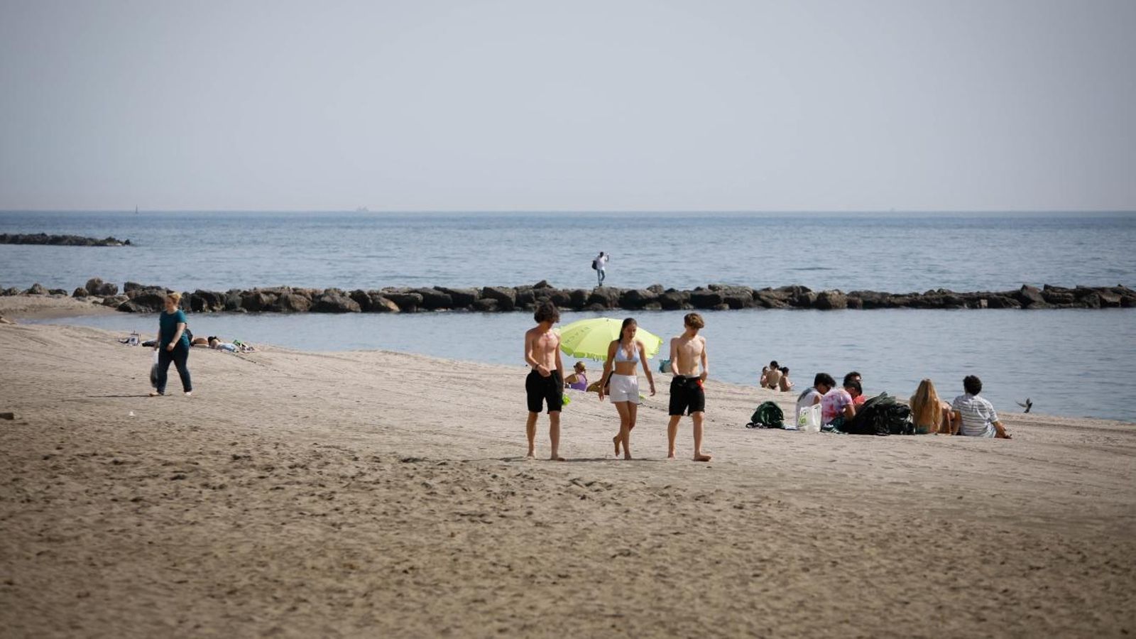 Unos chavales andando sobre la arena de la playa.