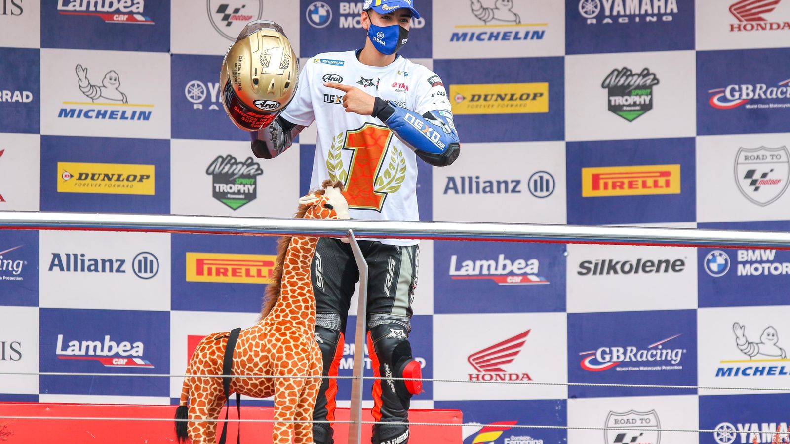 Borja Gomez, en el podio con una jirafa de peluche, camiseta con el '1' y casco personalizado.