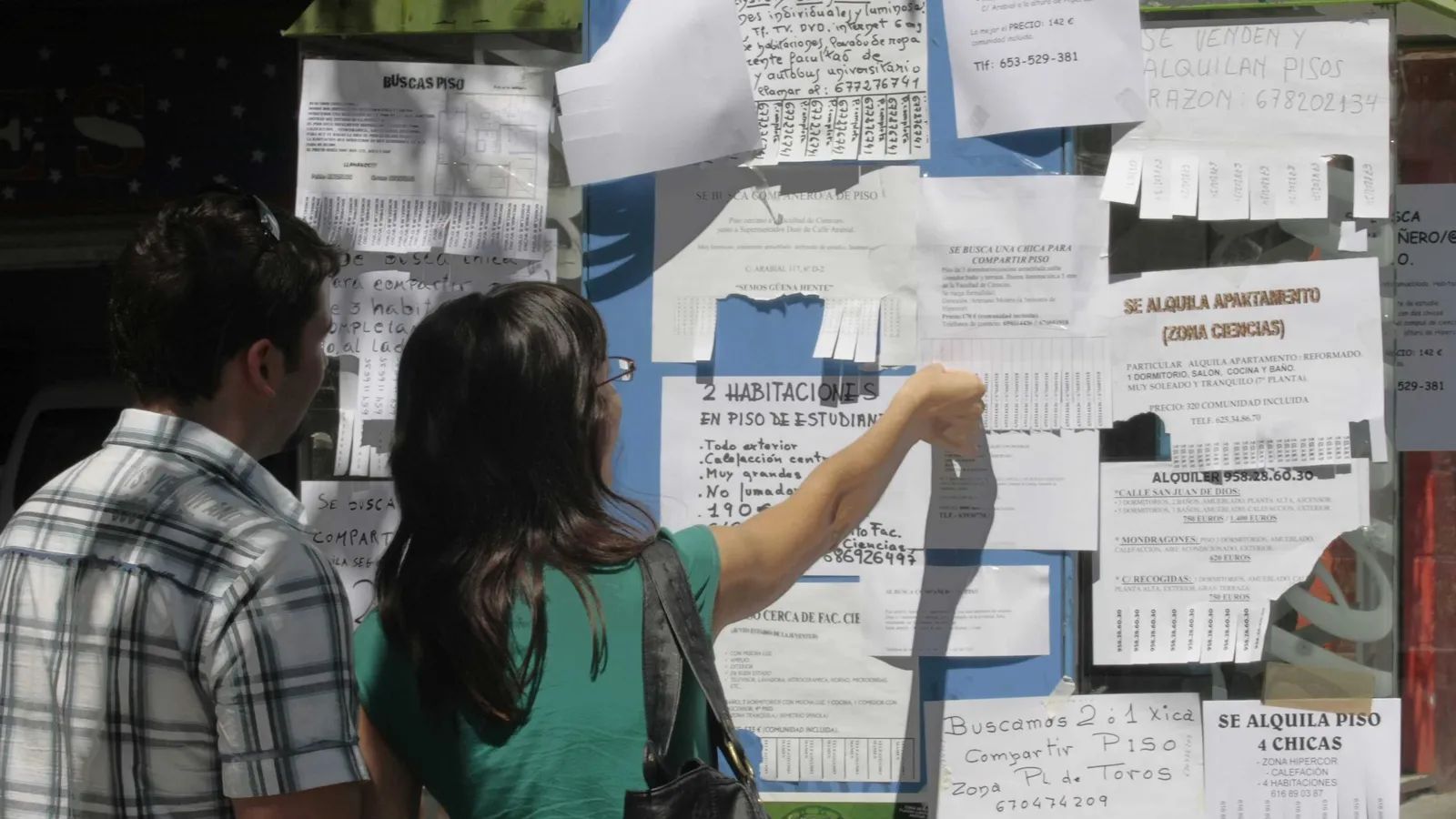 Dos personas buscan piso en tablones de la calle.