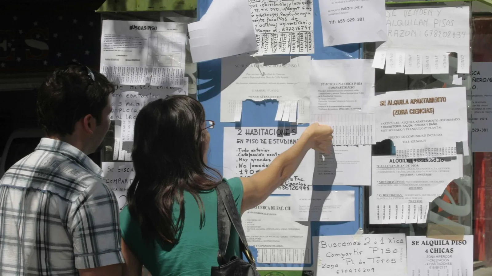 Dos personas buscan piso en tablones de la calle.