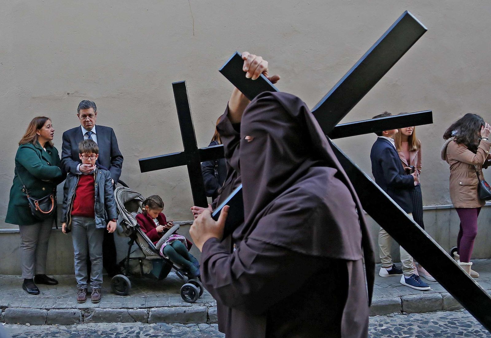 Penitentes de la cofradía de la Sagrada Lanzada con el antifaz echado hacia atrás y con la cruz al hombro siguen al misterio de la hermandad carmelitana.