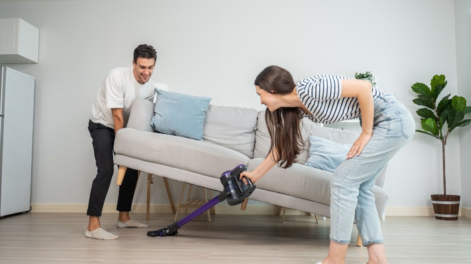 Dos jóvenes colaboran para limpiar su piso compartido con la aspiradora