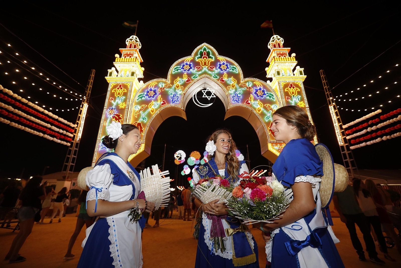 La salinera mayor junto a dos de las salineras de este año ante la portada ya iluminada de la Feria.