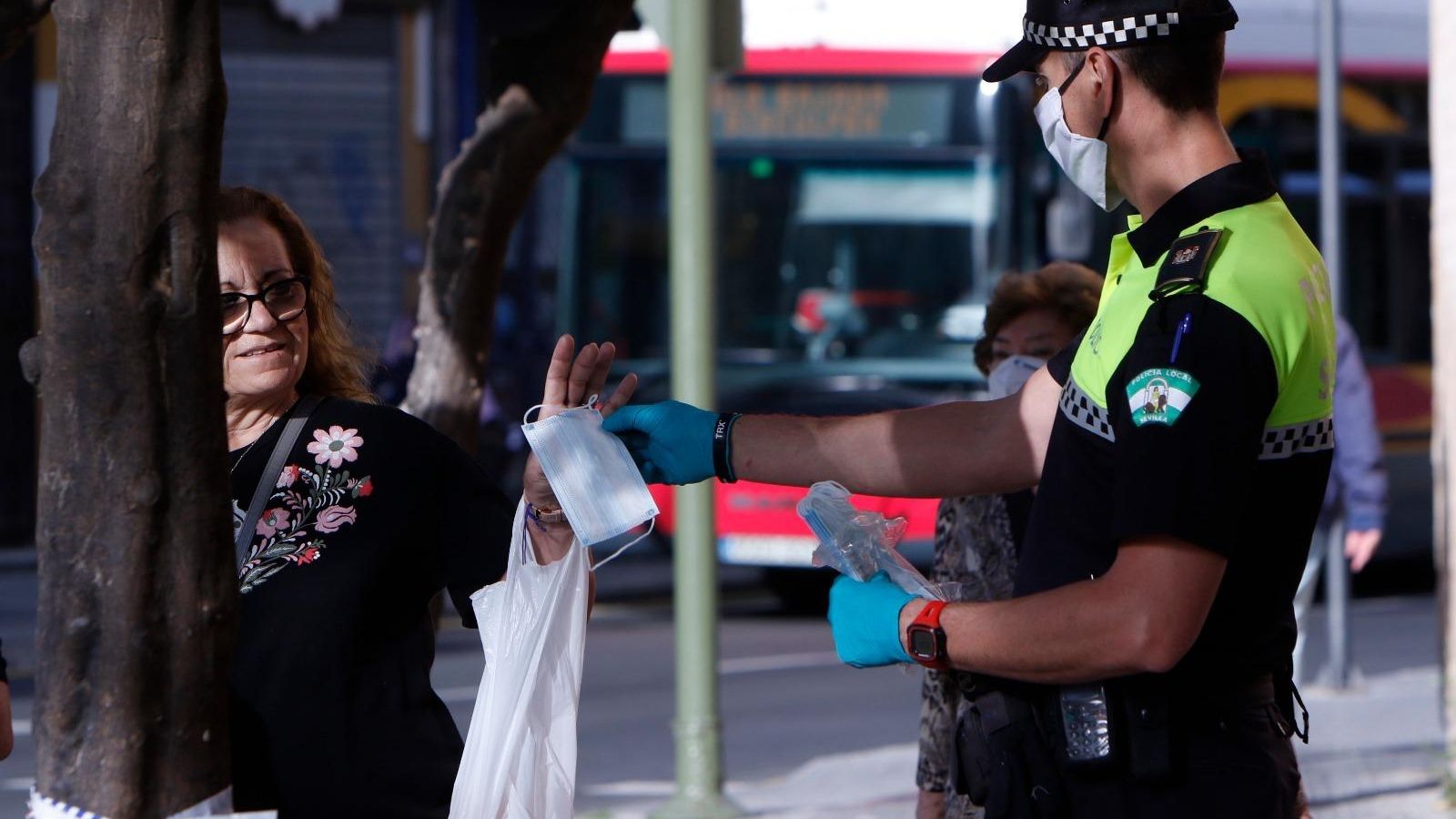 Un policía local entrega a una viandante una mascarilla.
