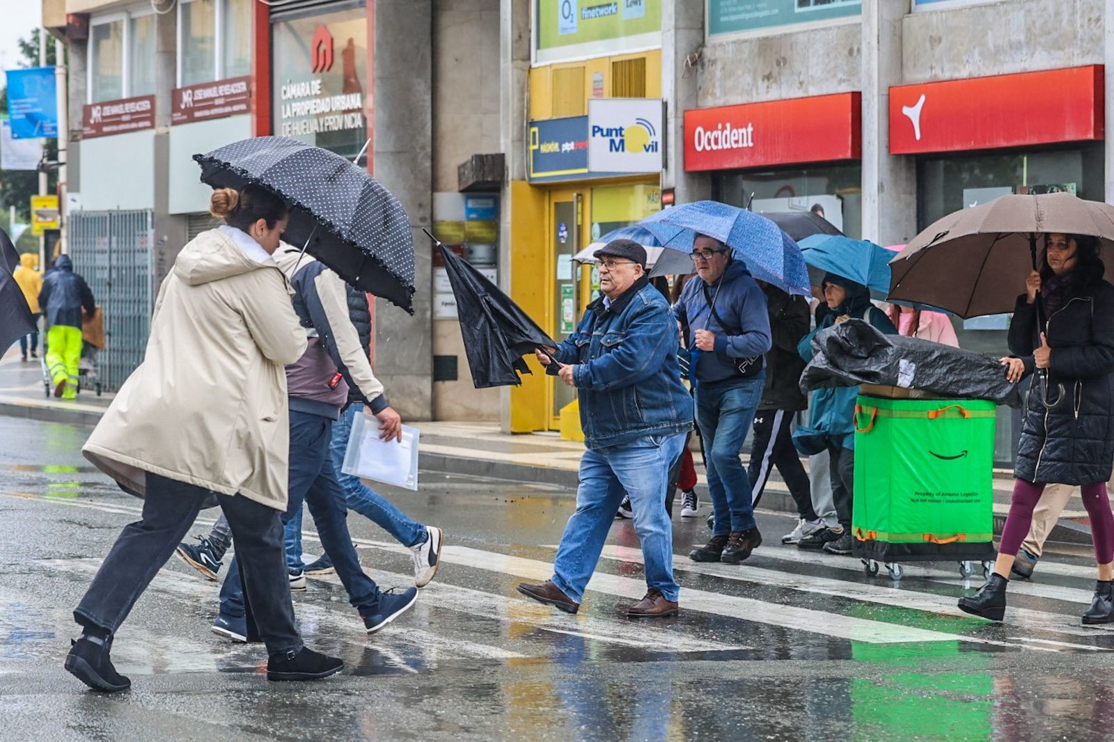 Varias personas con paraguas en las calles de Huelva se resguardan de un chubasco.