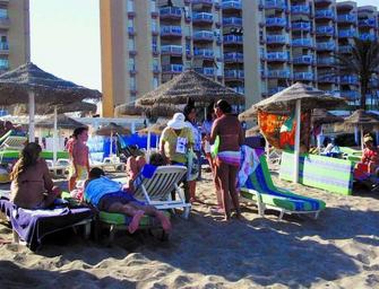Una masajista, con sombrero blanco, ofrece sus servicios en una playa de Fuengirola.