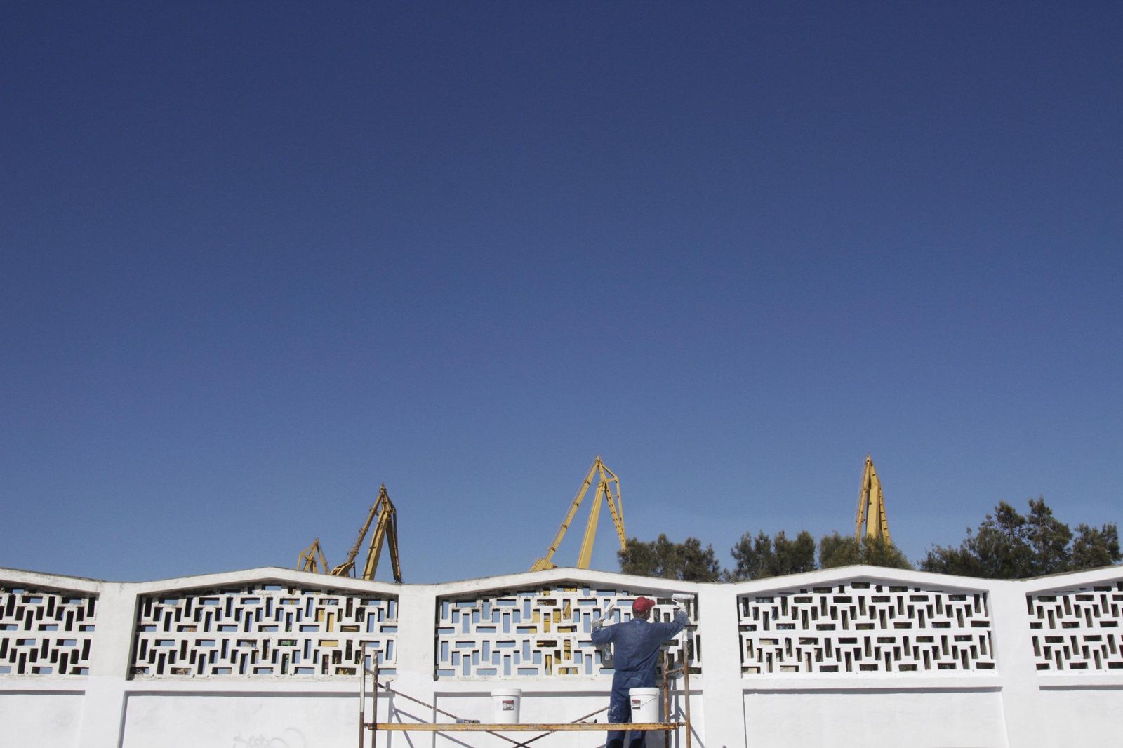 Un operario pinta, en una imagen de archivo, el muro de la carretera de Astilleros, más o menos en el lugar en el que habrá que abrir la cancela para el paso del futuro tren que llegará hasta la nueva terminal de contenedores del puerto de Cádiz