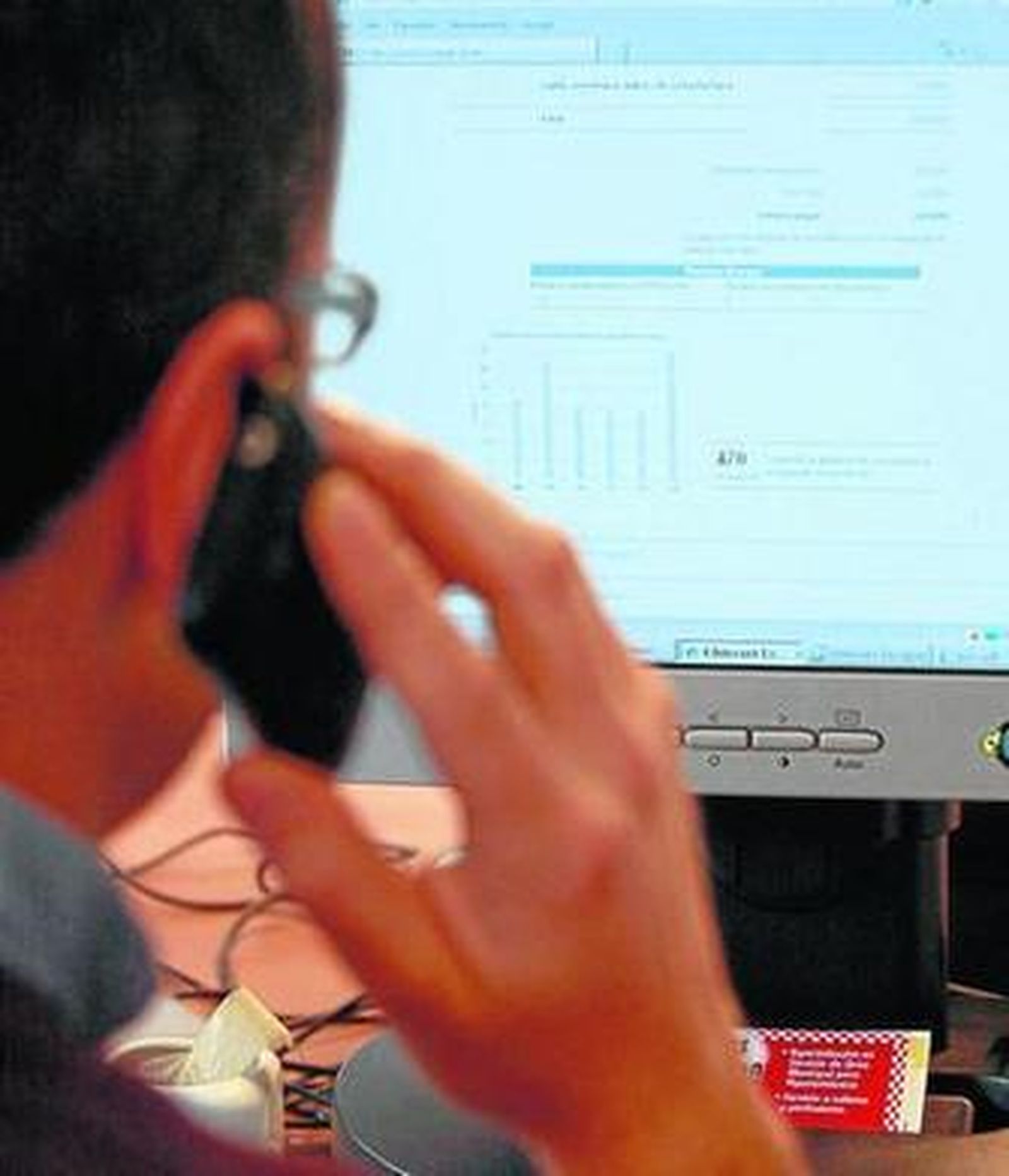 Un usuario habla por teléfono mientras consulta una factura en el ordenador.