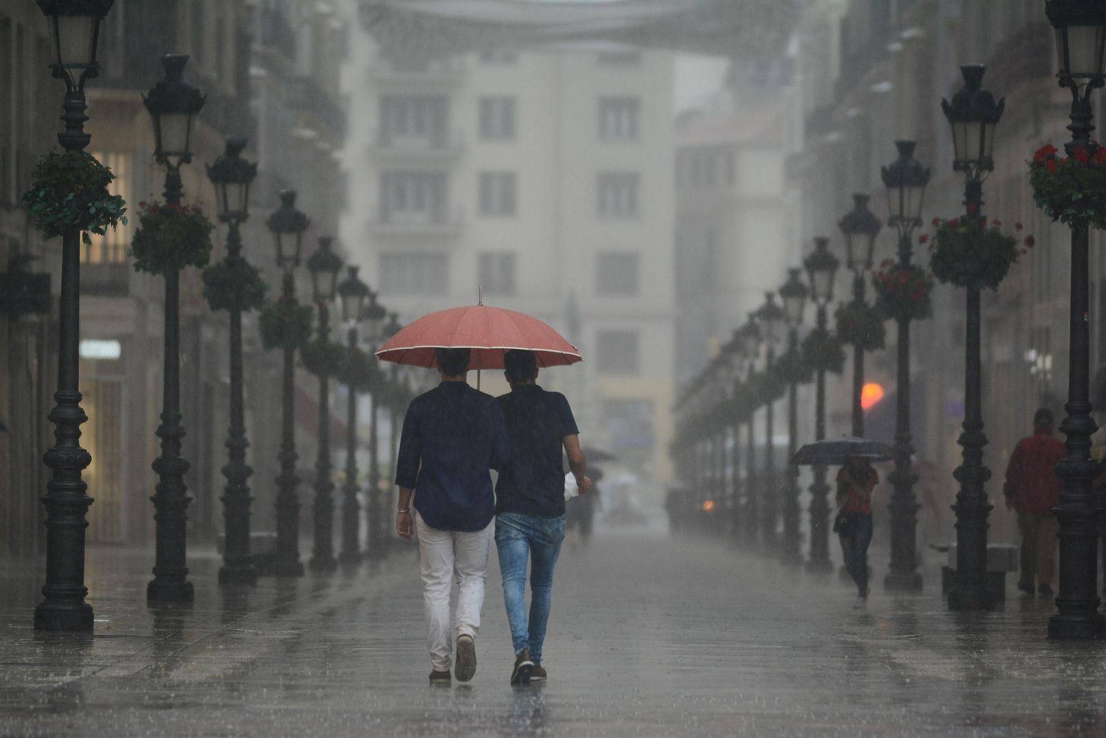 Dos jóvenes pasean por la calle Larios durante la tormenta