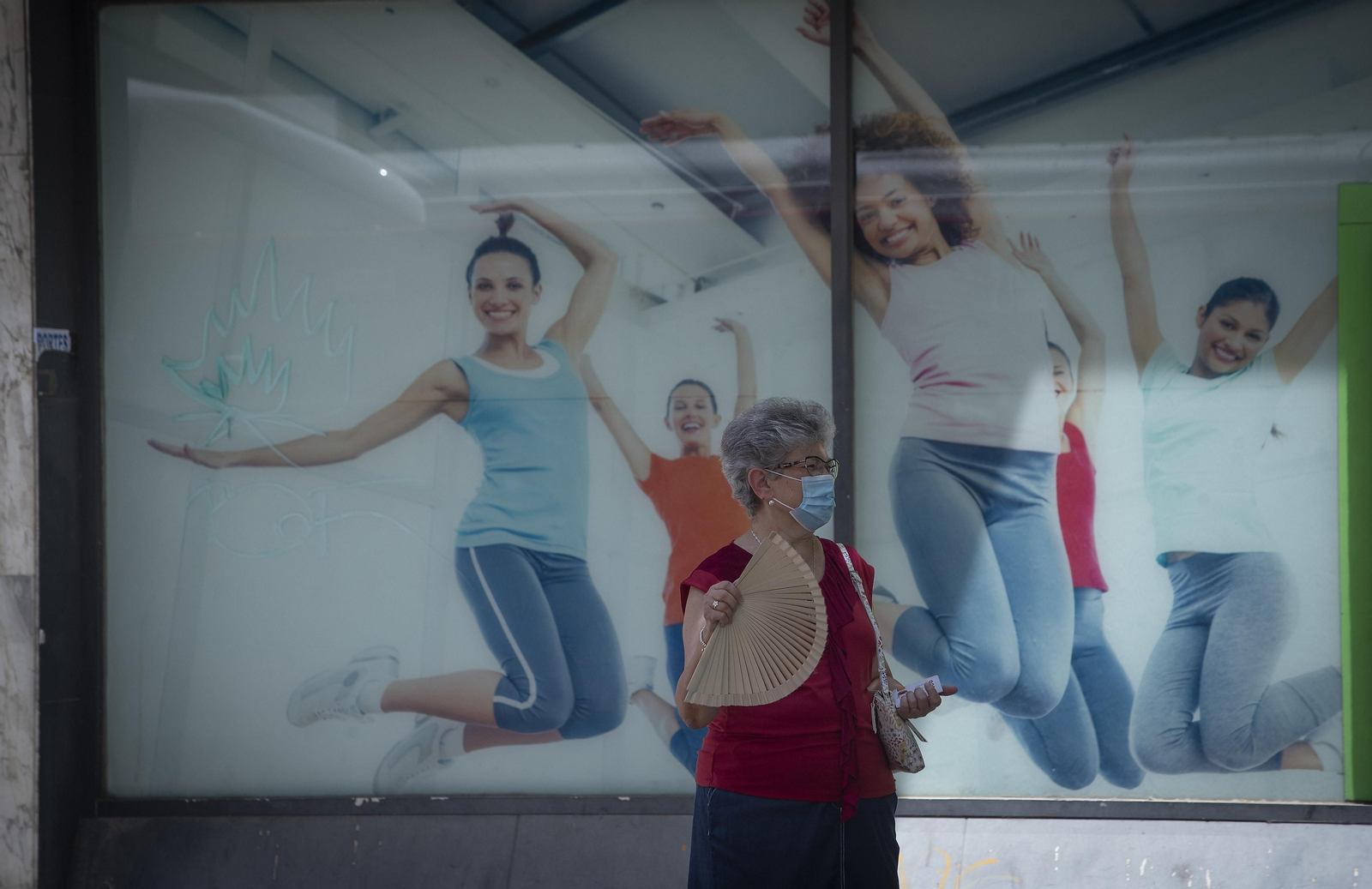 Una mujer se abanica a su paso por un escaparate.