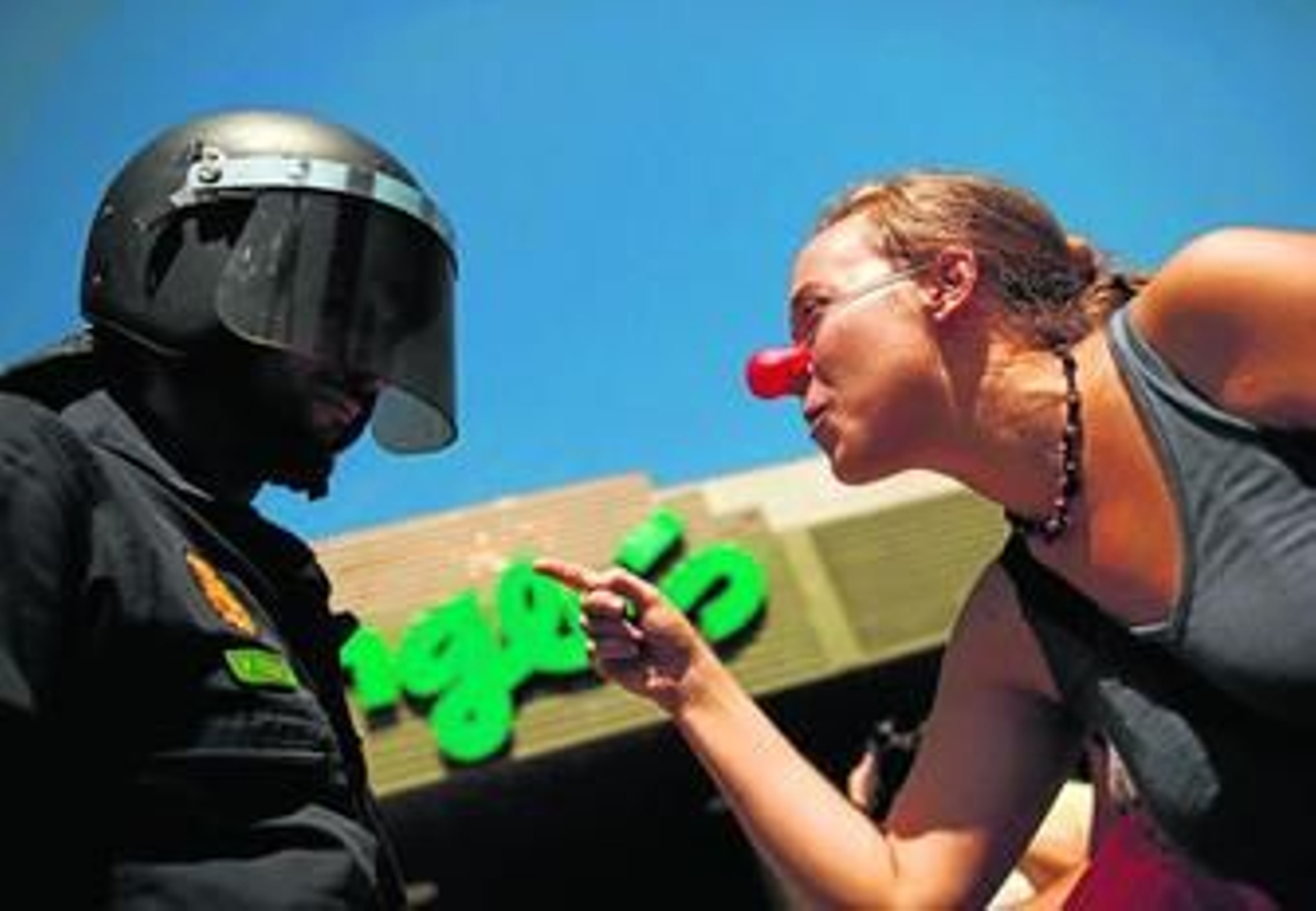 Una chica tocada con nariz de payaso se enfrenta a un agente de la Policía Nacional frente a unos grandes almacenes.