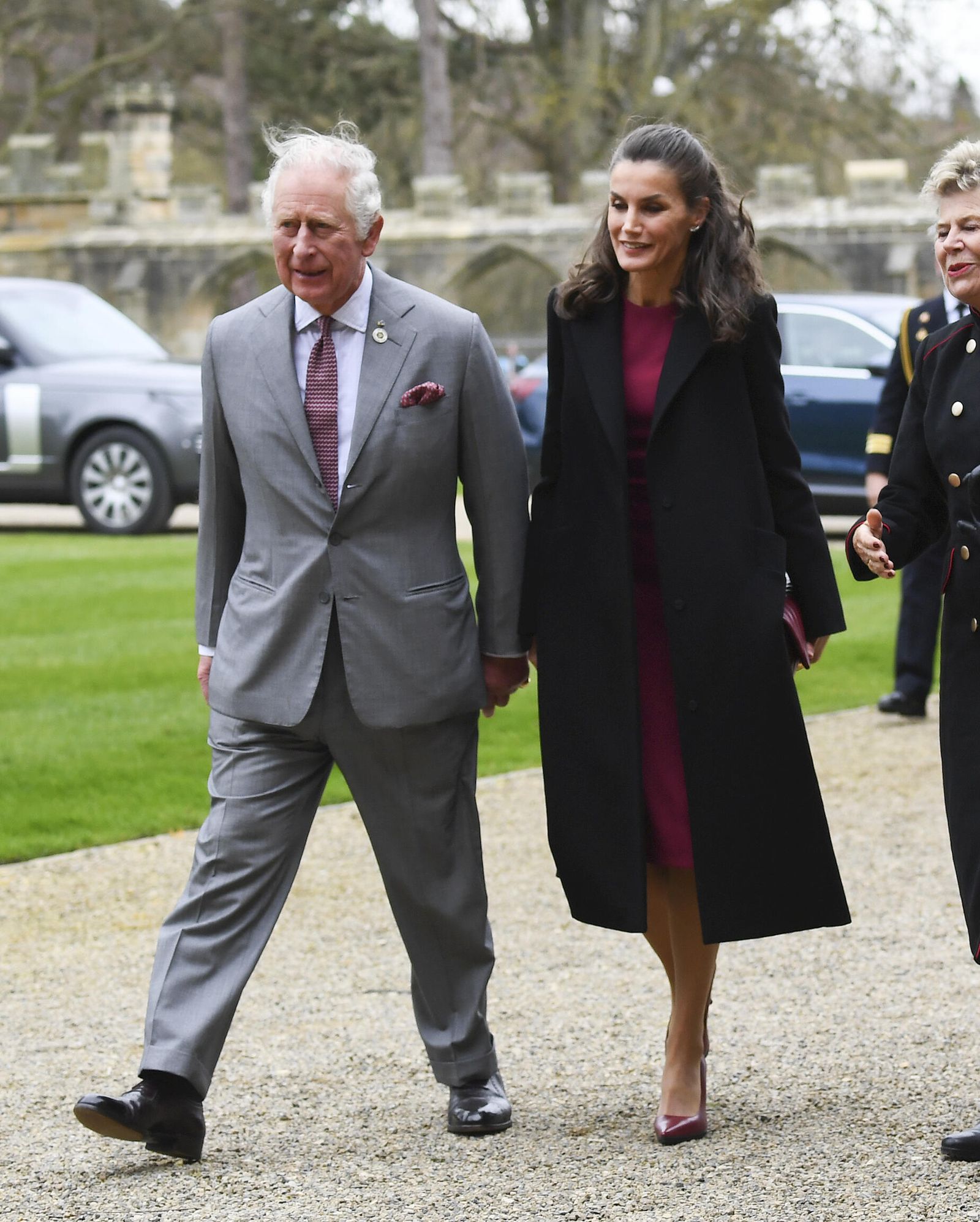 La Reina, acompañada del príncipe de Gales, con vestido rojo y abrigo negro durante su visita a Durham.