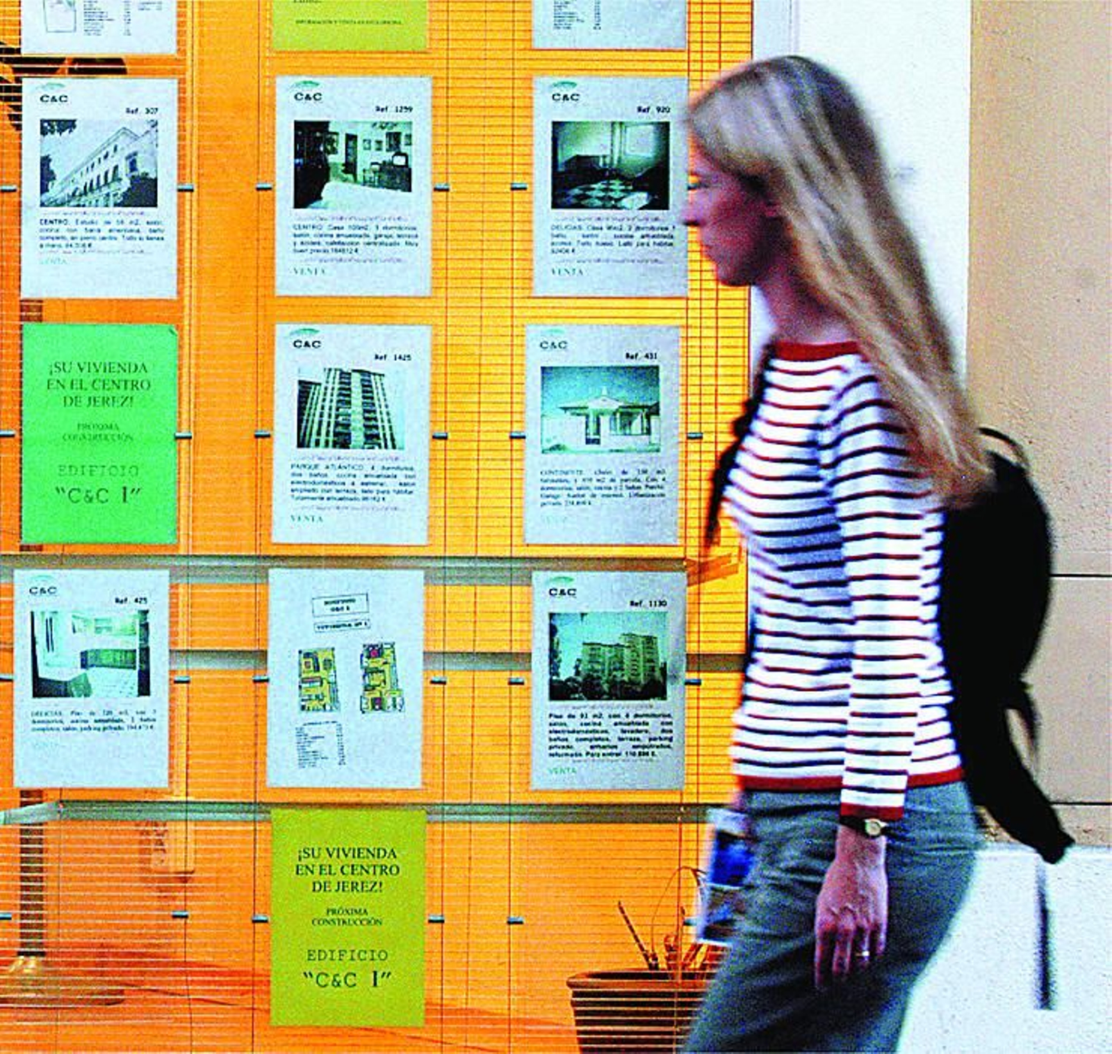 Una joven pasa ante el escaparate de una inmobiliaria repleto de ofertas de venta y alquiler.