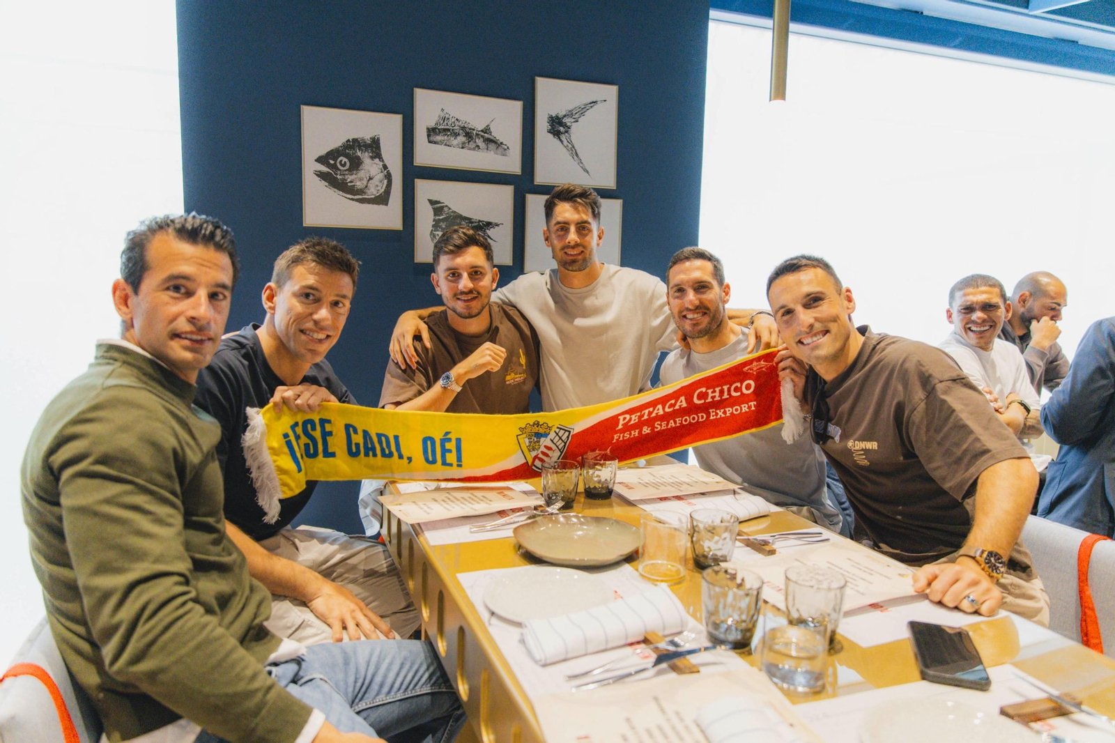 Posado de un grupo de jugadores con una bufanda que agrupa al Cádiz CF y a Petaca Chico.