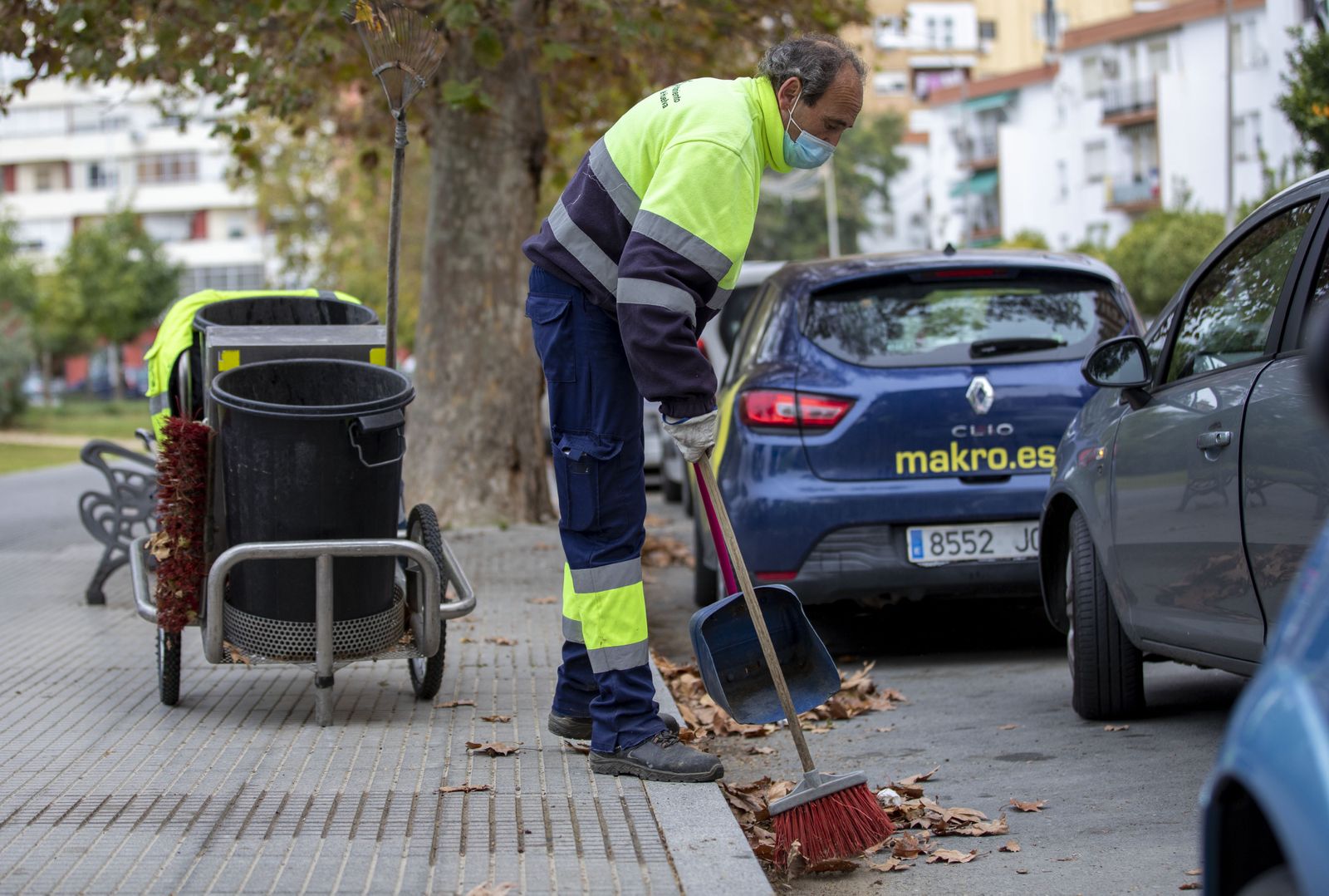 Un operario de limpieza recoge hojas caídas de árboles.