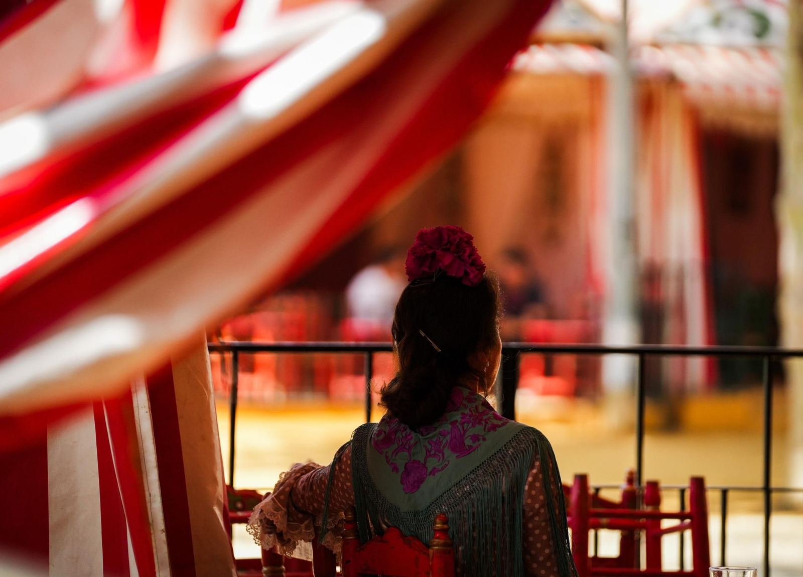 Mujer vestida de flamenca observa desde una caseta