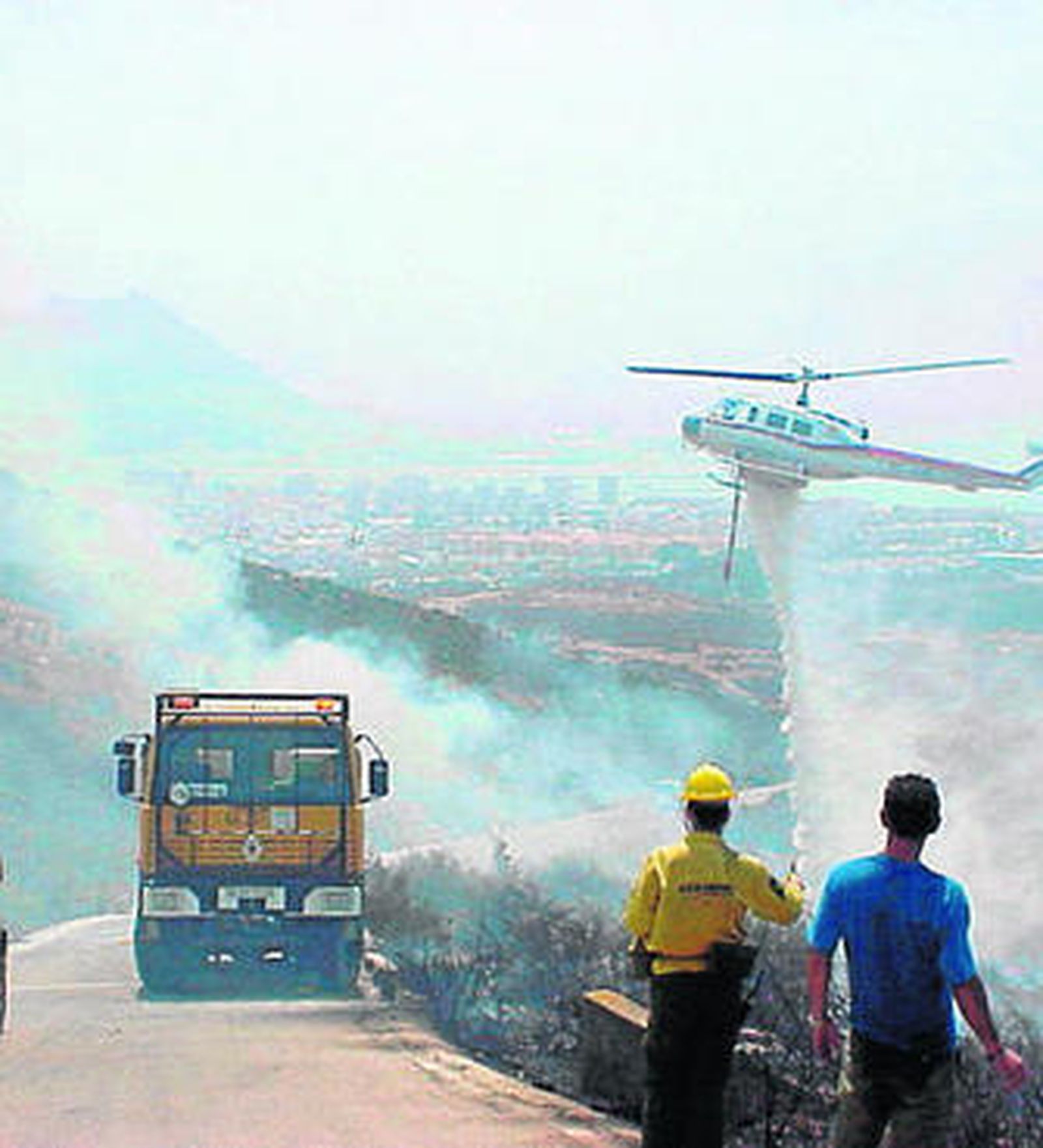 Dos voluntarios observan a los efectivos del Infoca en su intervención en un fuego en La Línea.