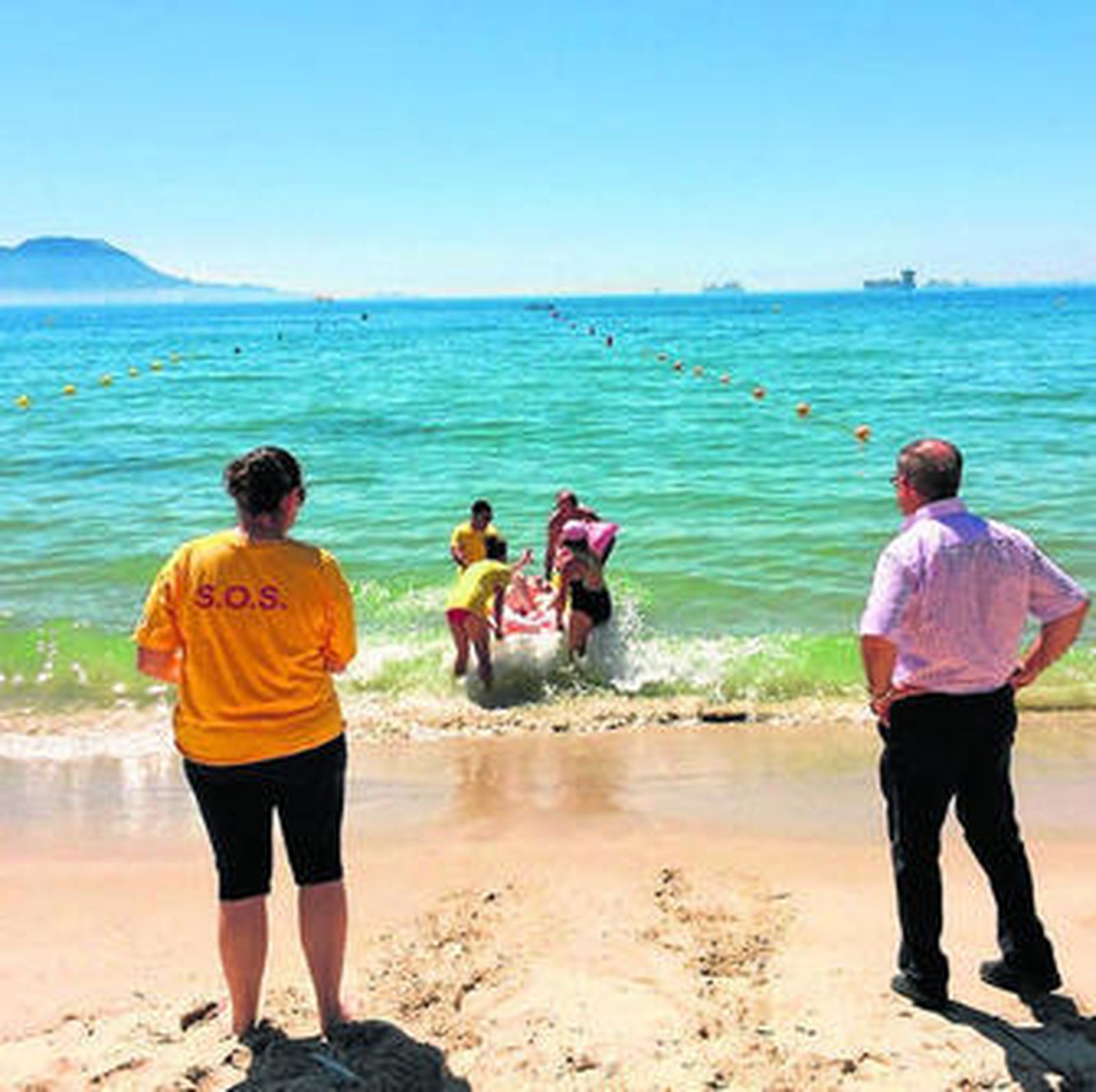 En la imagen, los socorristas introduciendo en el mar la camilla adaptada.