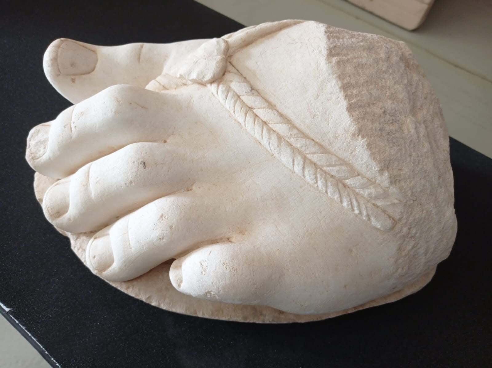 Pie femenino en mármol blanco con detalles de trenzado en la sandalia.