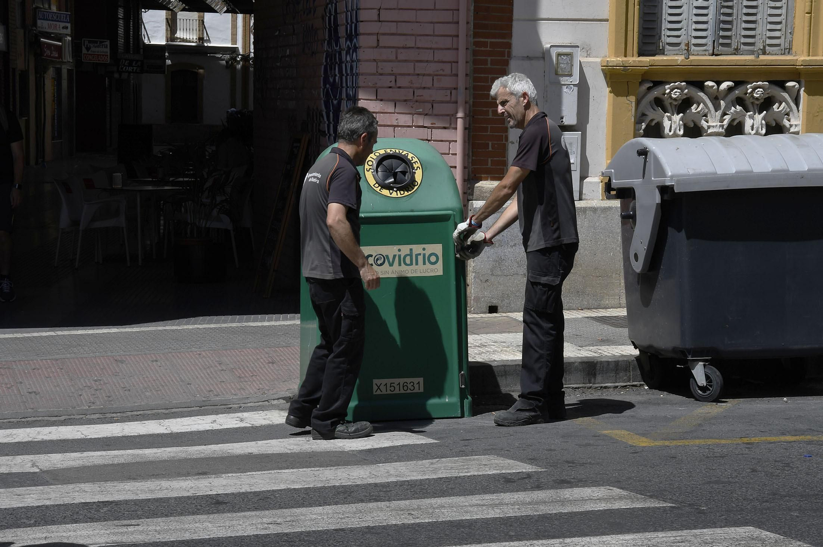 Dos operarios municipales junto a un contenedor de vidrio en la capital onubense.