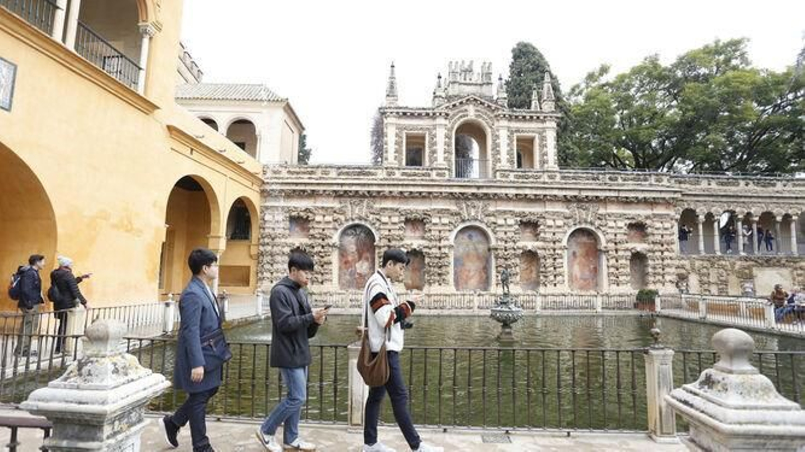 Tres jóvenes pasan ante el Estanque de Mercurio del Alcázar.
