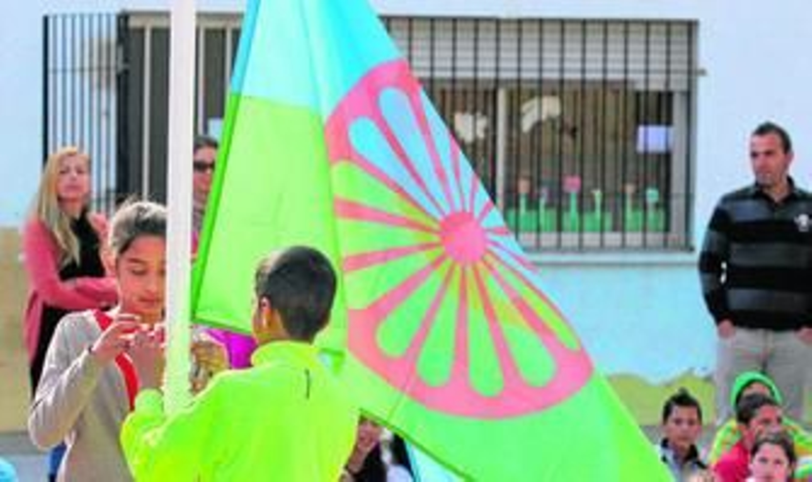 Dos niños izan la bandera en el patio del centro público de la barriada de La Palmilla.