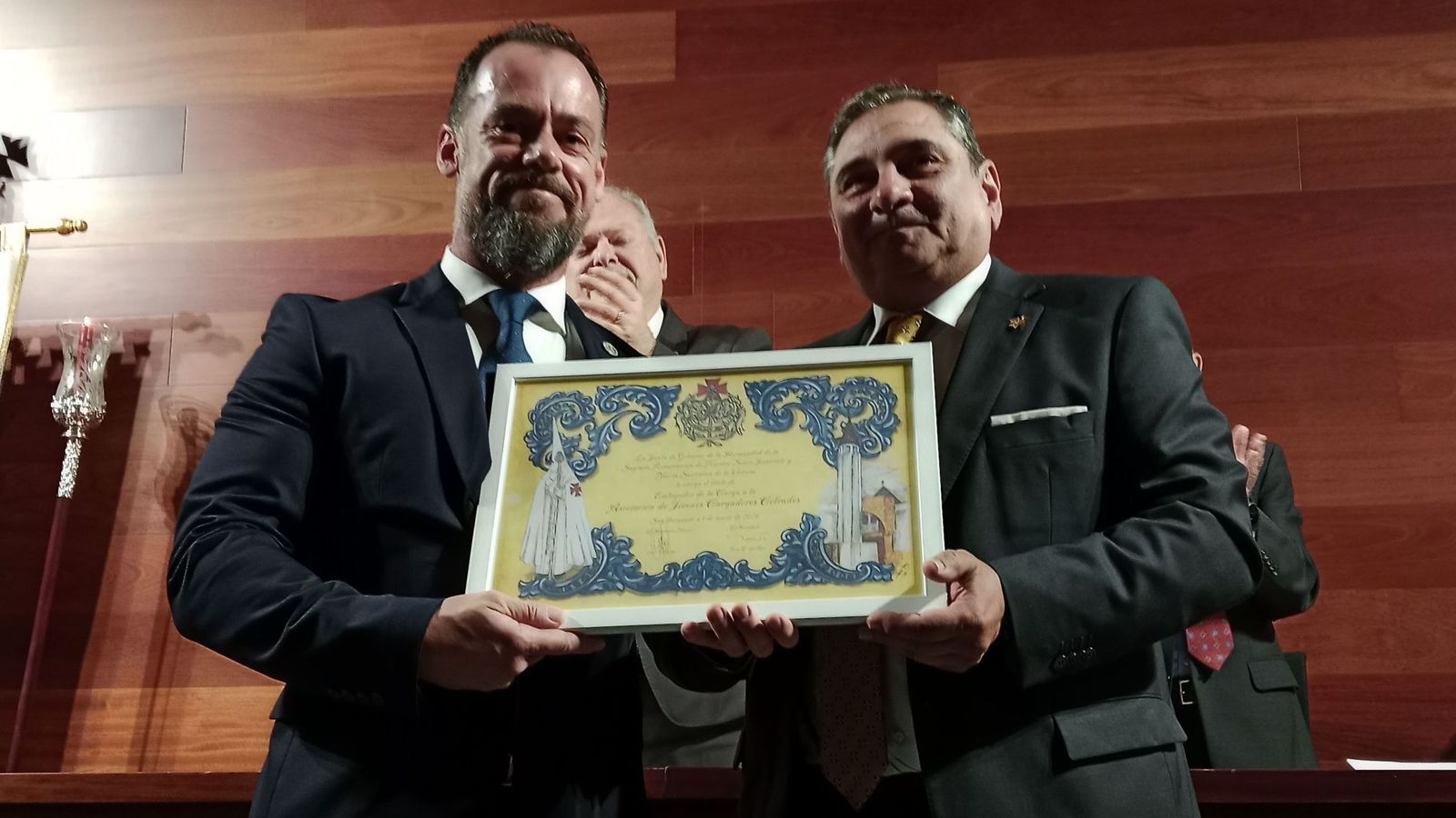 El presidente de la asociación Jóvenes Cargadores Cofrades (JCC), Juan Pérez Barrionuevo, recoge el título de Embajadora de la Carga Isleña de manos del hermano mayor de la Resurrección, José Antonio Faiña, en San Fernando