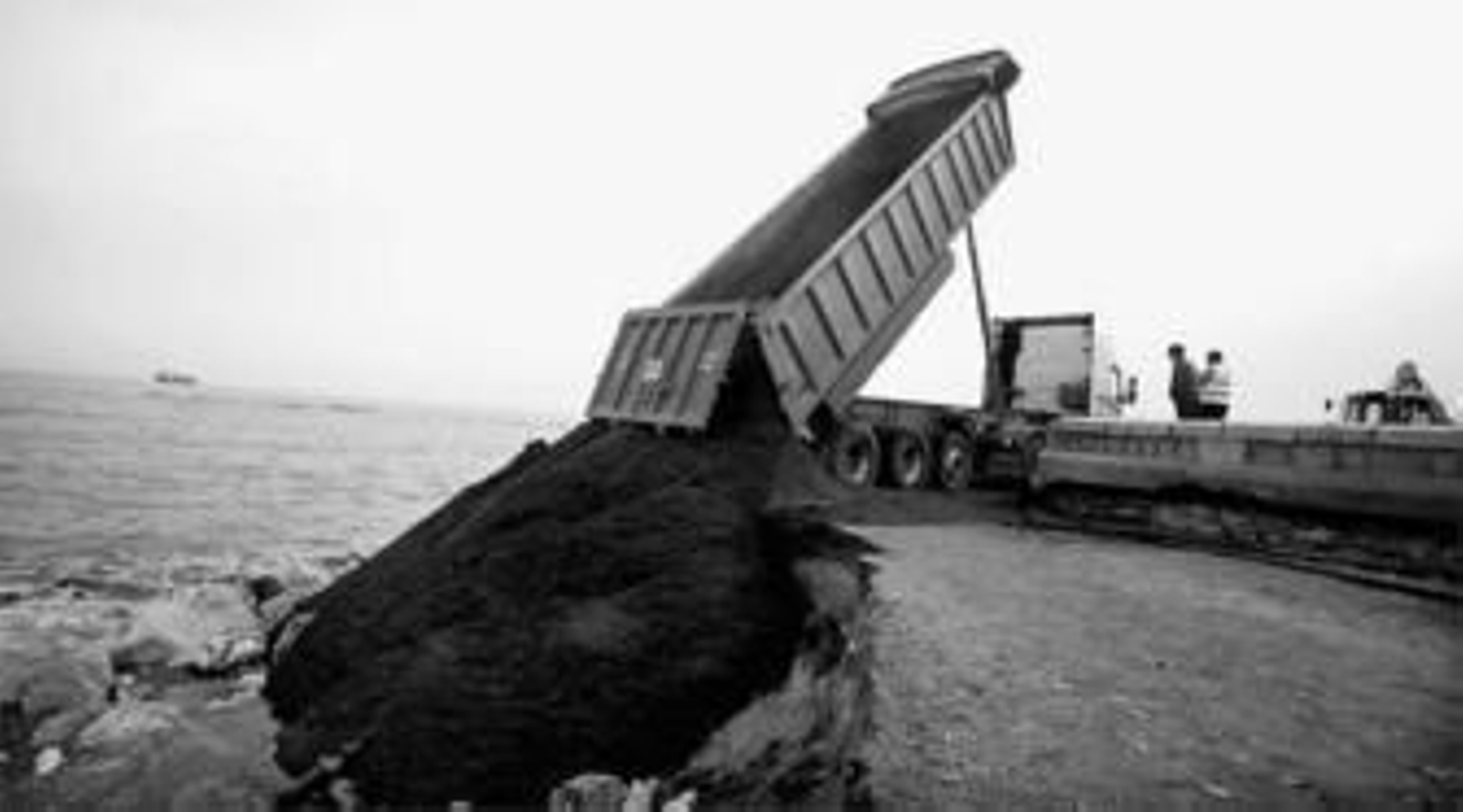 Un camión descarga varias toneladas de arena en la playa de La Caleta, en Málaga capital.