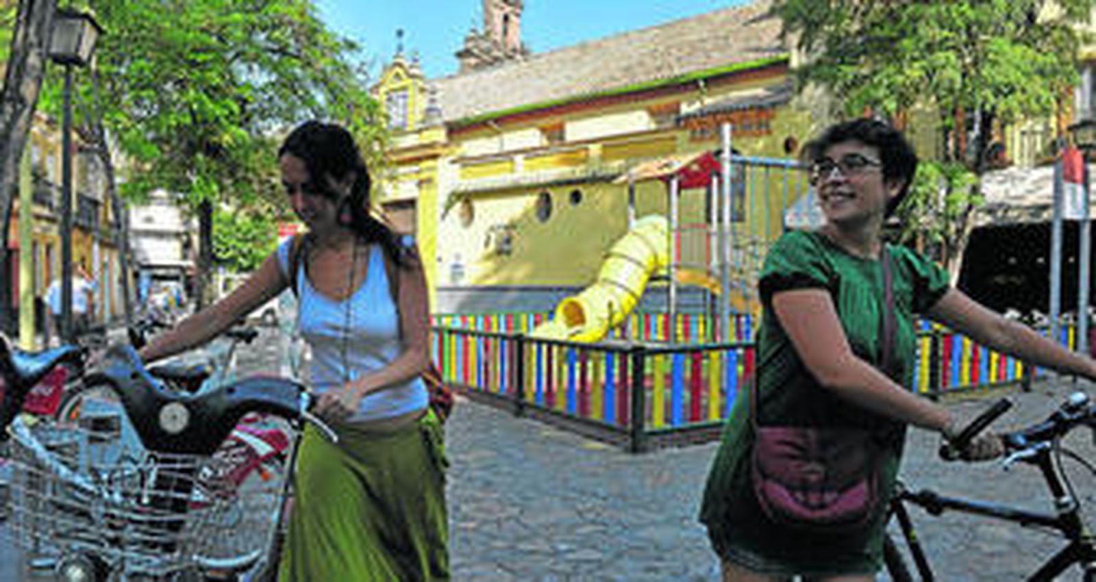 Los bicicleteros de Sevici y los columpios en los que juegan los niños de la plaza de San Juan de la Palma.