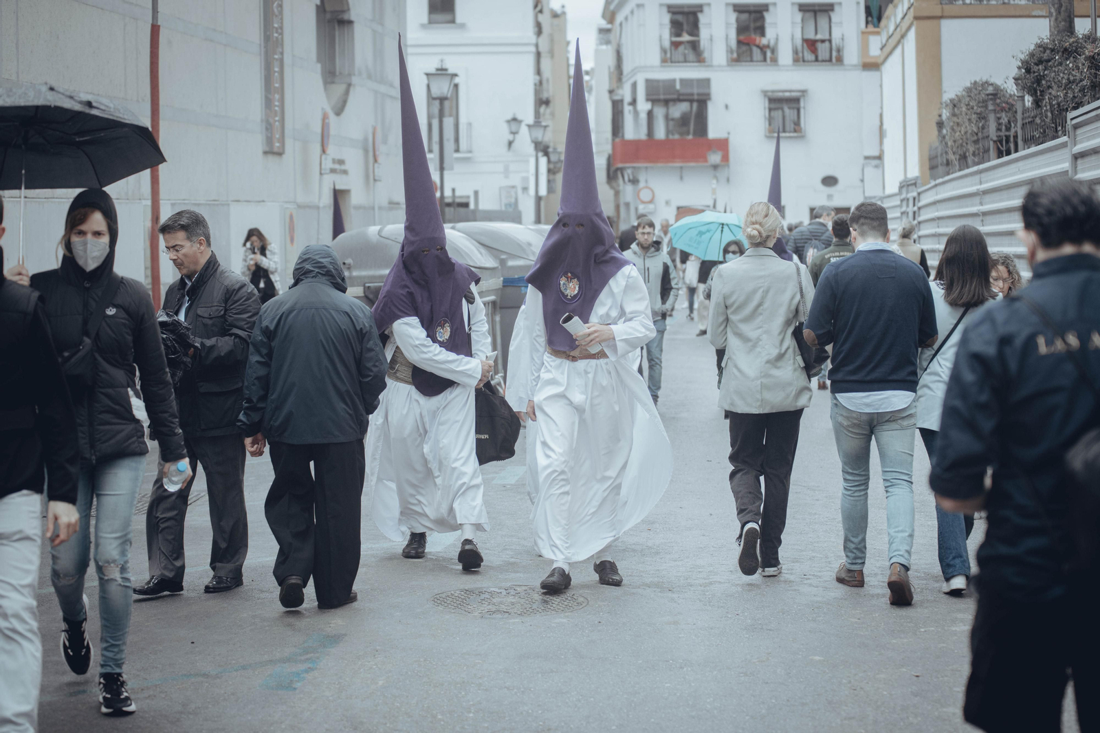 Dos nazarenos caminan entre varias personas por el centro de la ciudad.