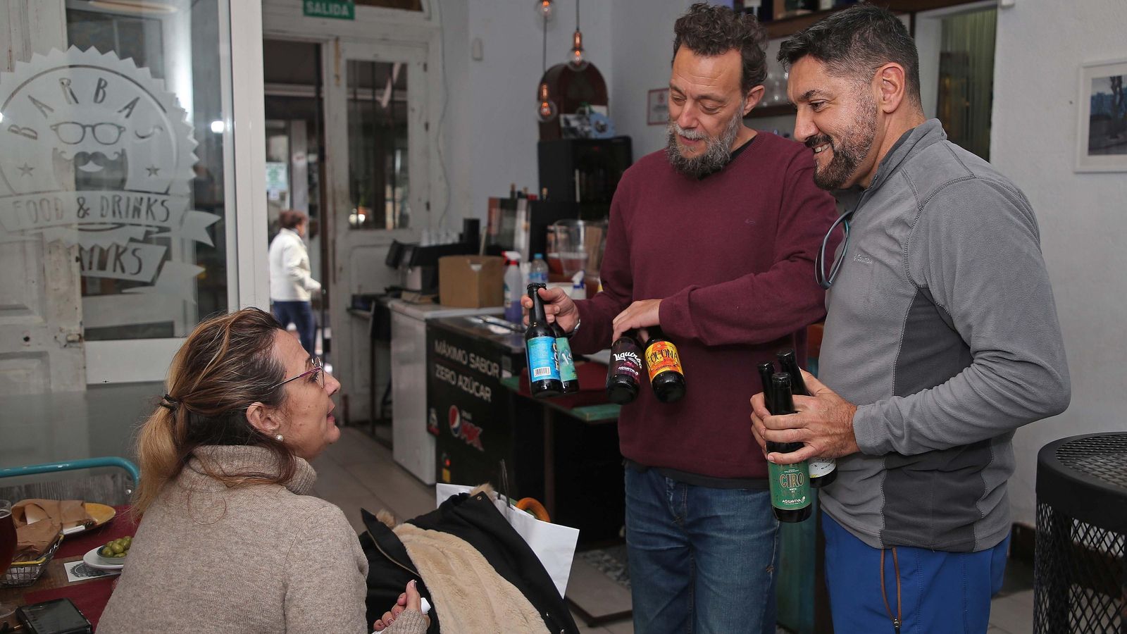 Sergio y David le muestran las cervezas a una clienta.