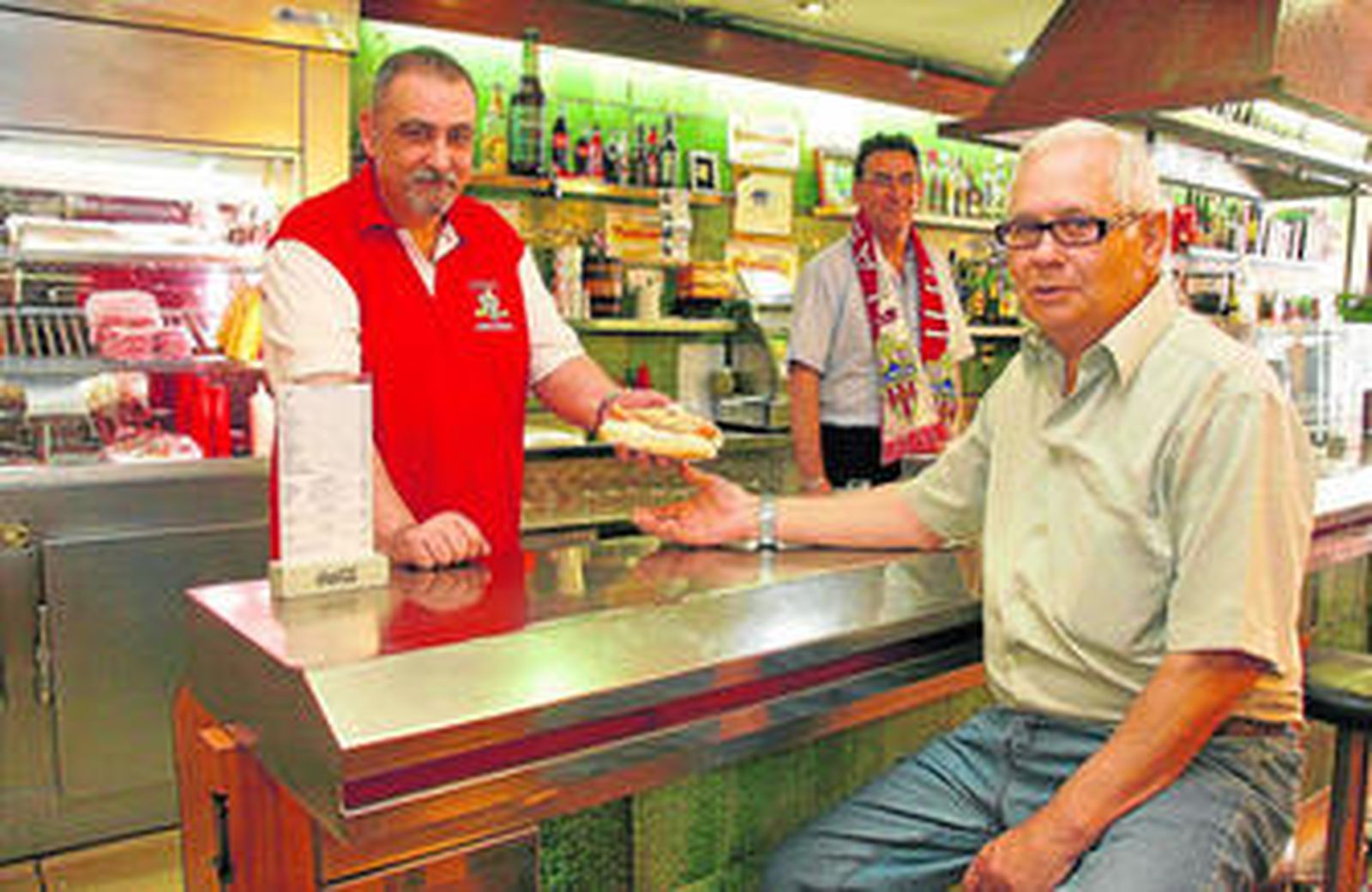 Pepe y Andrés le sirven un perrito caliente, especialidad de la casa, a José. Los dos primeros son de Nacimiento, el tercero de Doña María.