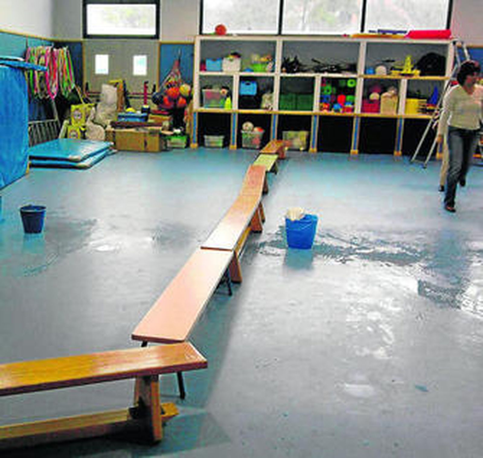 Imagen de la sala de usos múltiples, encharcada y con cubos bajo cada gotera.