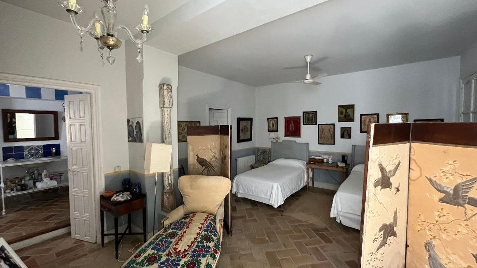 Un dormitorio con dos camas decapadas junto a una colección de exvotos y pareja de biombos.