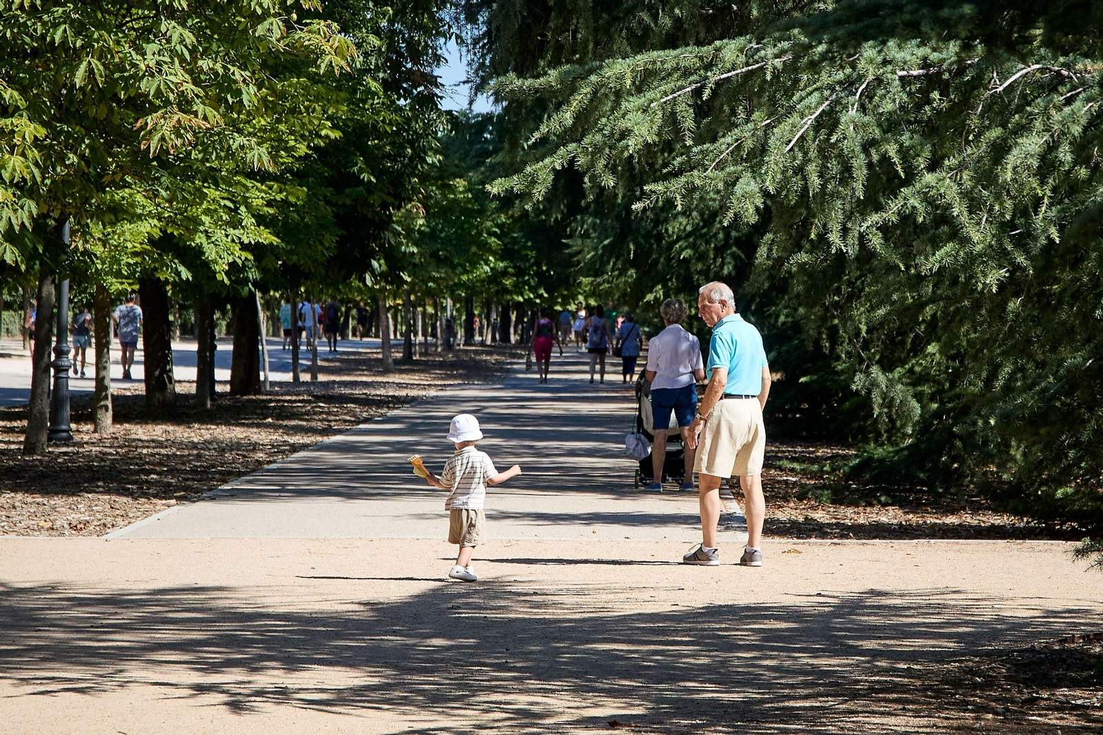 Un hombre pasea por el parque a un pequeño que empuña varios juguetes en su mano izquierda.