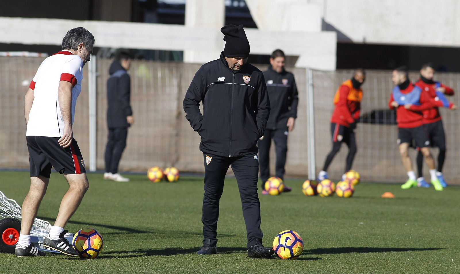 Jorge Sampaoli permanece pensativo sobre el césped mientras su ayudante Juanma Lillo, mucho menos abrigado, juega con un balón.