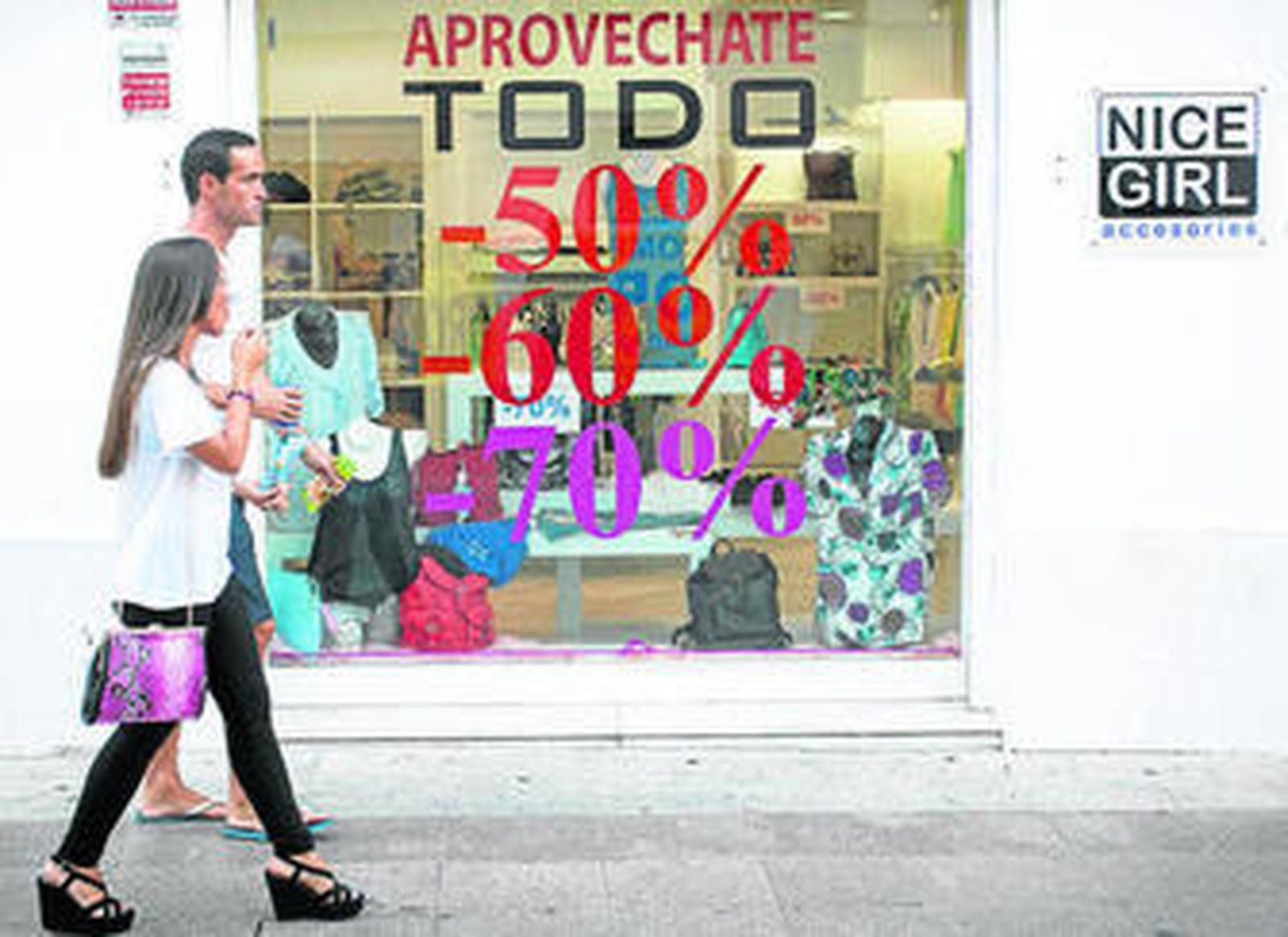 Dos jóvenes pasan ante un escaparate en el que se anuncian rebajas.