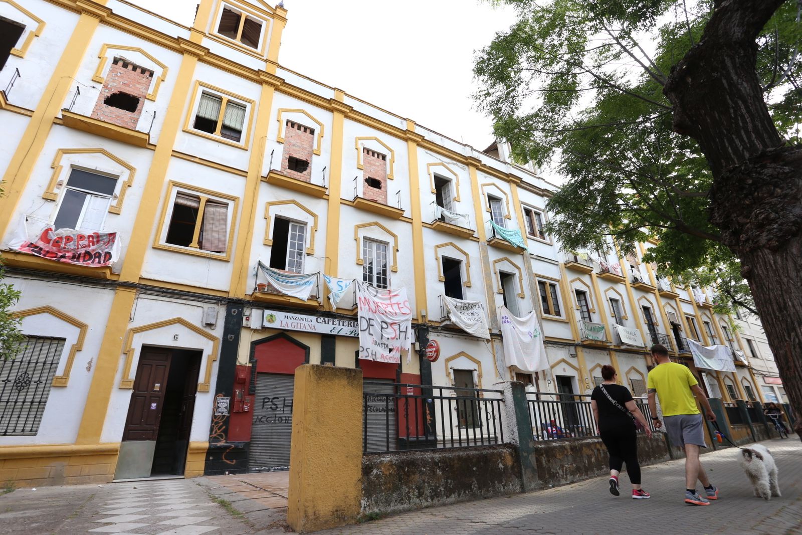 Una pareja con su perro pasa delante la fachada del inmueble.