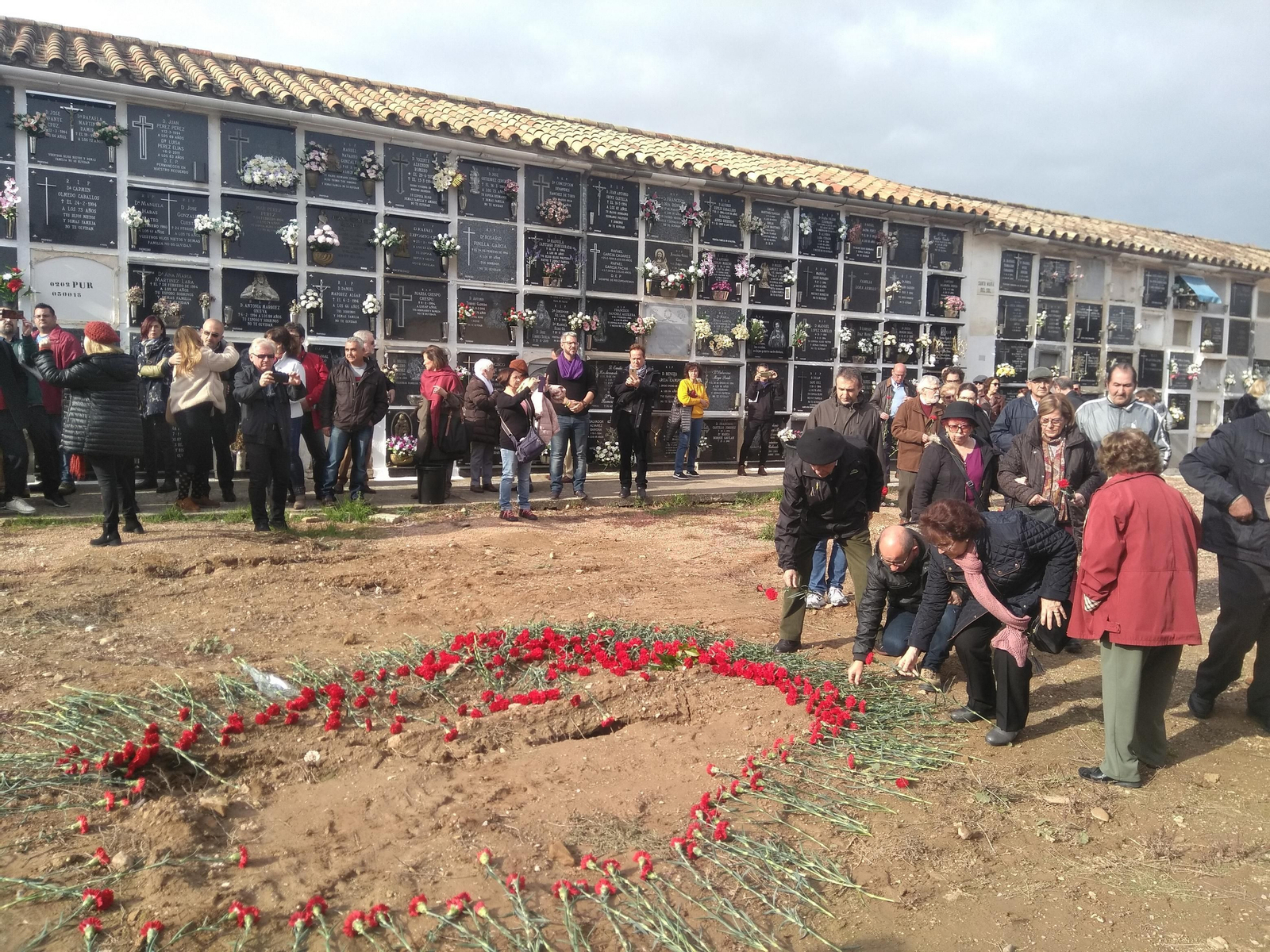 Varias personas depositan flores en el lugar de la fosa común del cementerio de  la Salud.