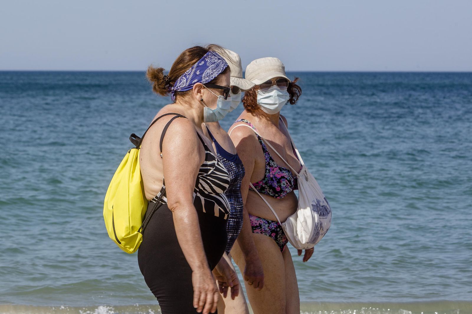 Mujeres pasean por una playa de Cádiz con mascarillas.