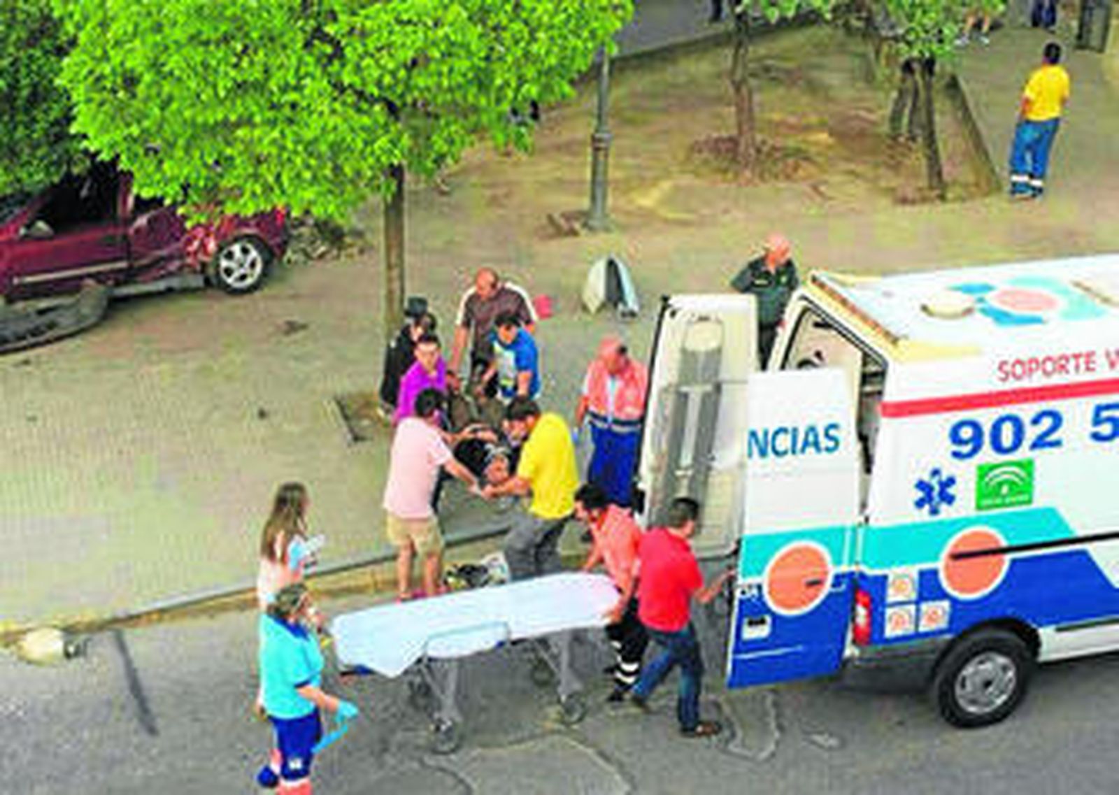 Uno de los heridos es trasladado a la ambulancia con el coche accidentado al fondo.