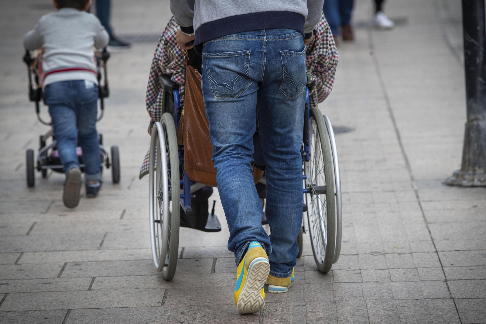 Una persona empuja la silla  de ruedas de una persona mayor.
