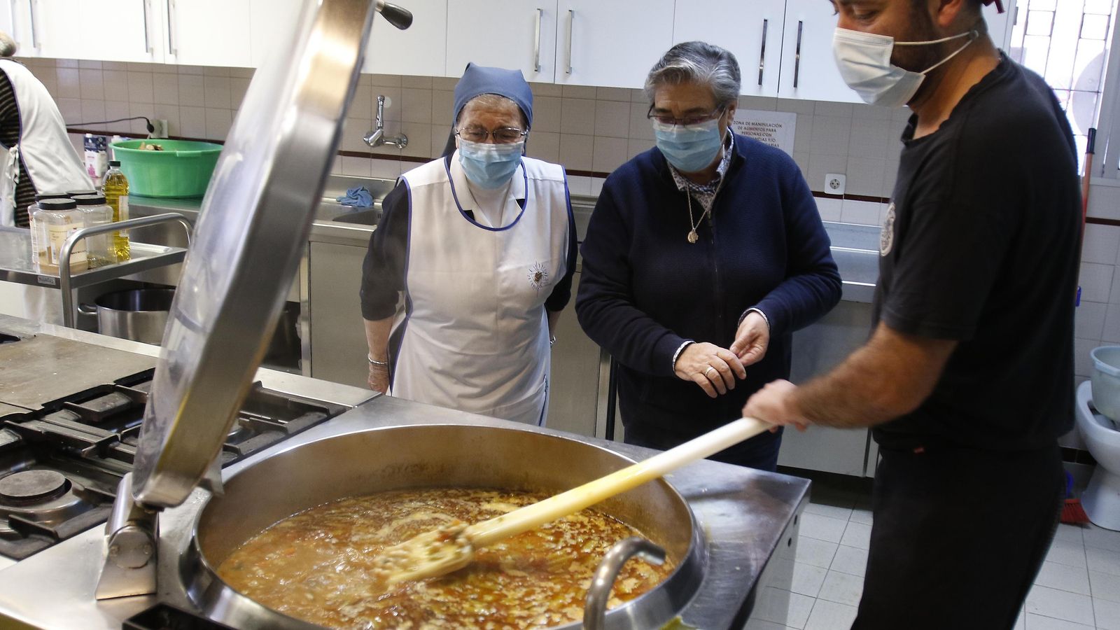 Un cocinero mueve el guiso en la cazuela ante la mirada de las hermanas.