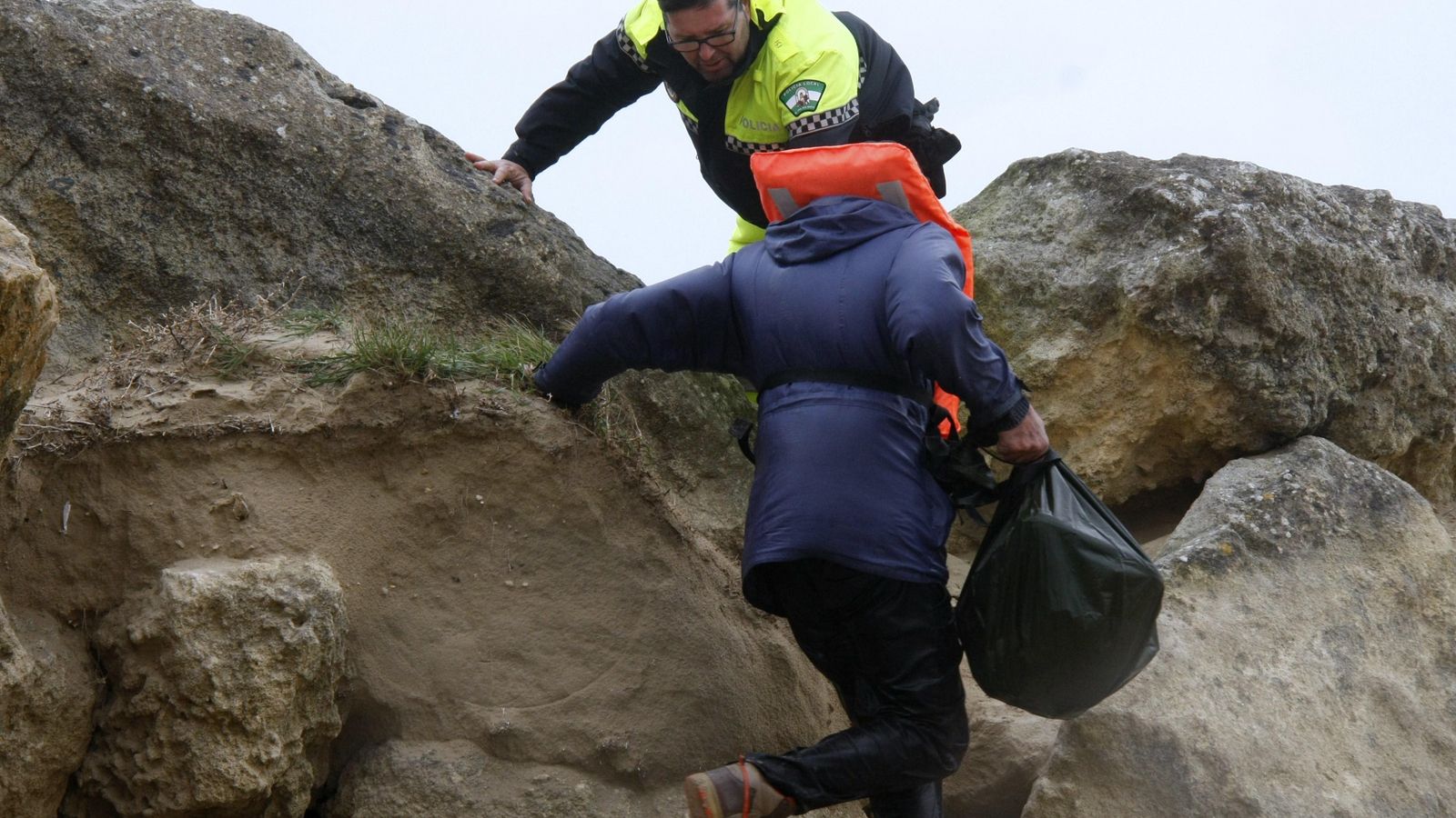 Un agente de policía ayuda a subir por las rocas al tripulante del velero.