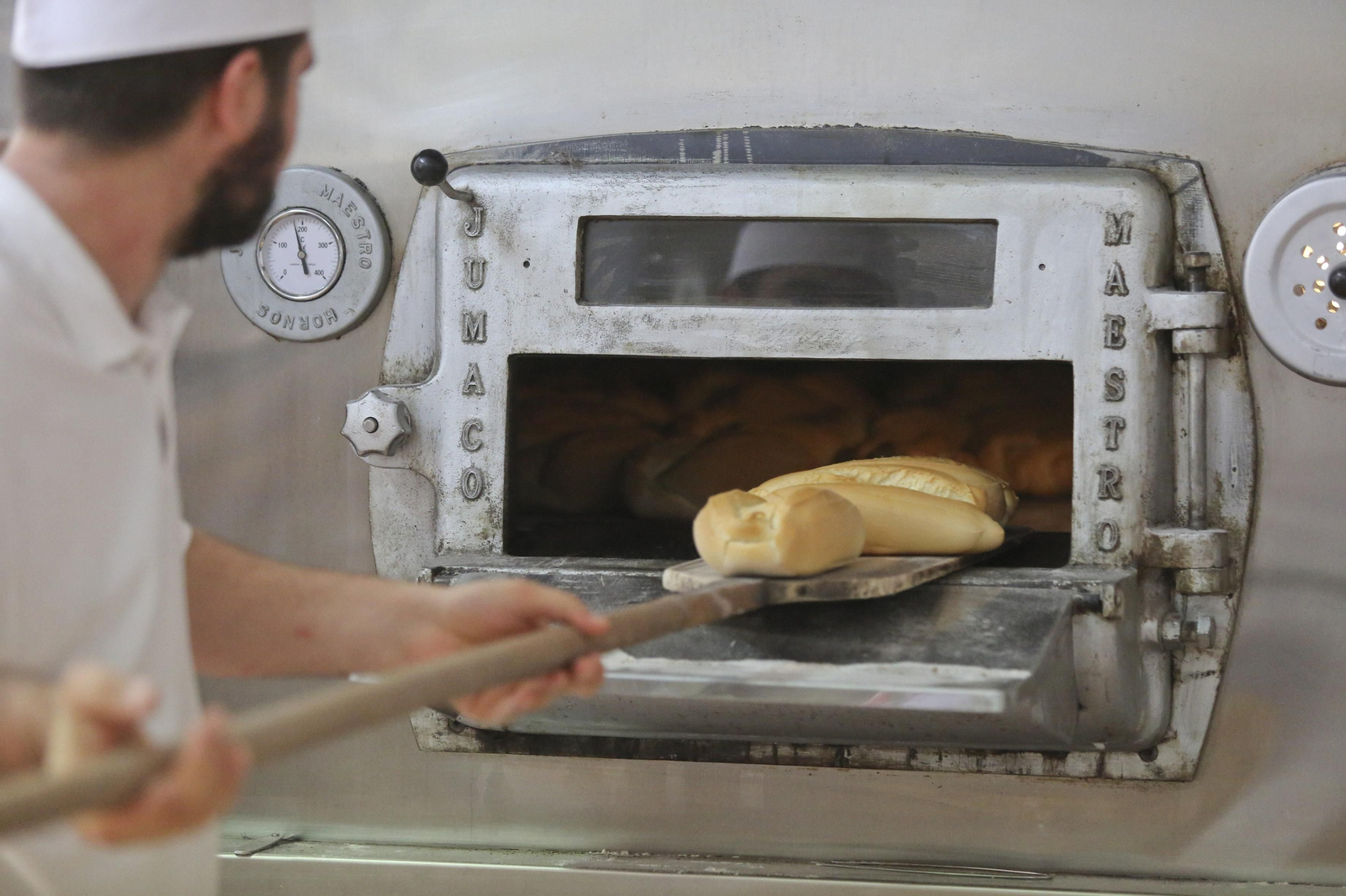 Un panadero saca del horno varios trozos de pan.