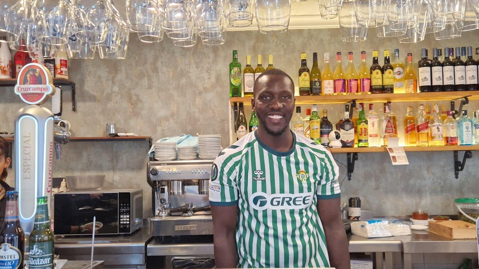 Moussa Niang, detrás de la barra como cocinero con la camiseta del Betis.