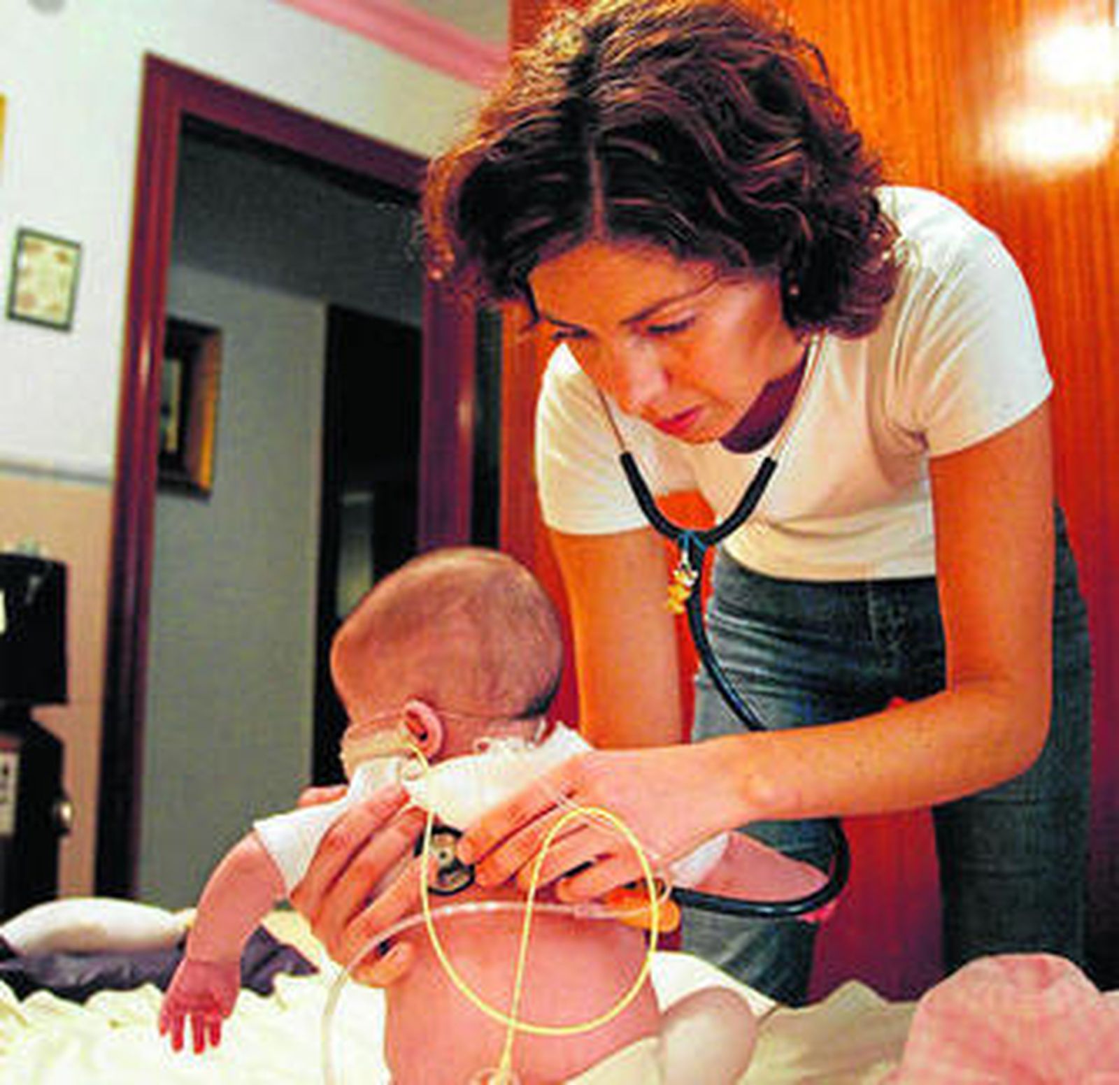 Una pediatra ausculta a un bebé en su domicilio.