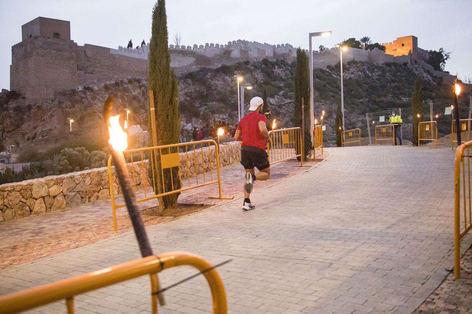 Un corredor avanza entre antorchas, con la Alcazaba de fondo.
