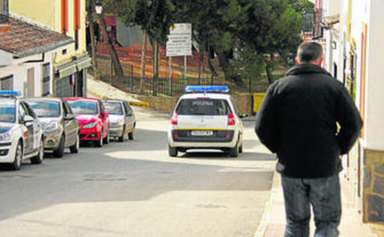 Un hombre camina, ayer, por una de las calles de Arriate ante la presencia de un vehículo de la Policía Local.