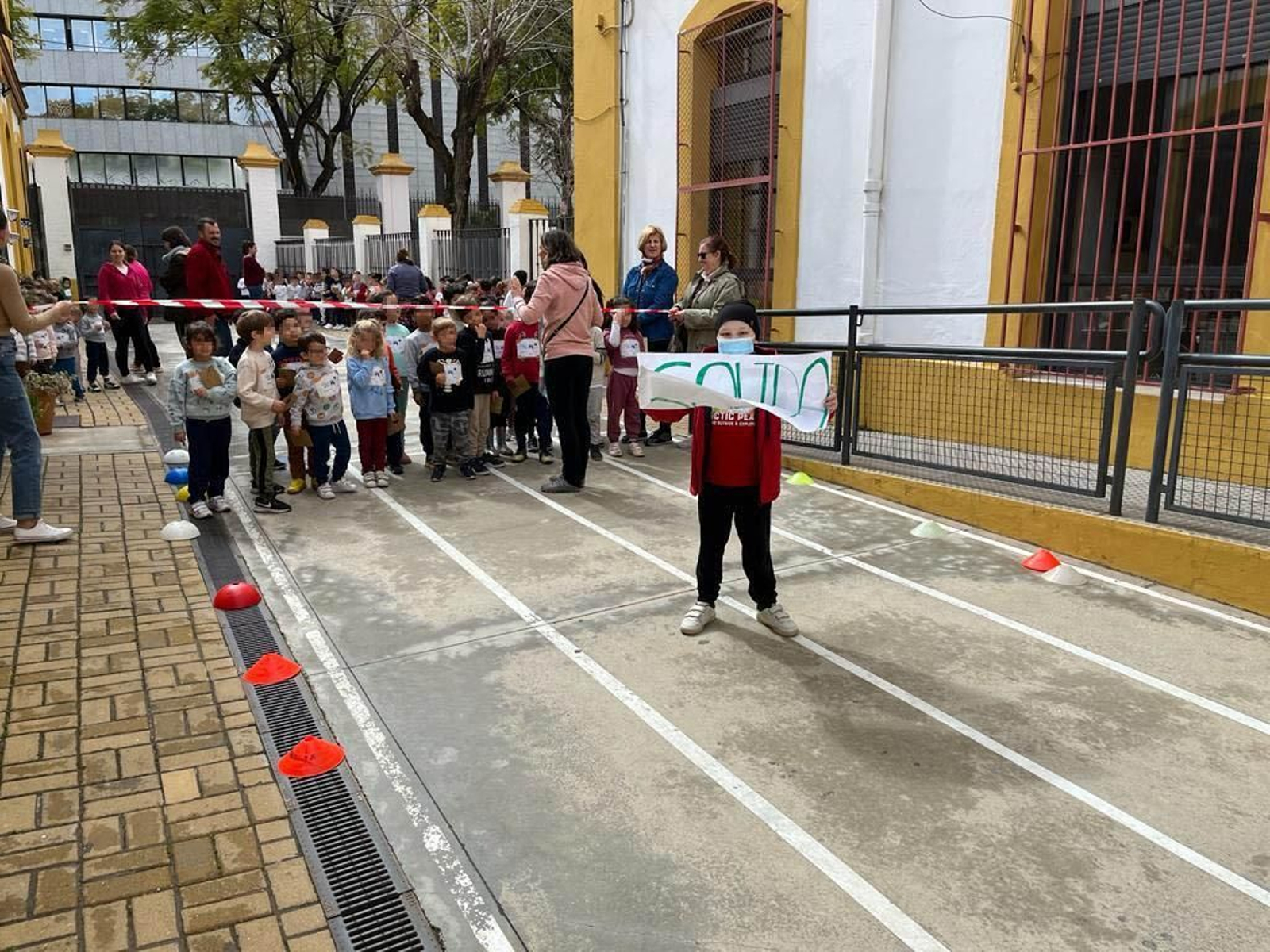 Gonzalo, con el cartel que indica la salida, mientras un grupo de alumnos del CEIP Borbolla esperan para correr.